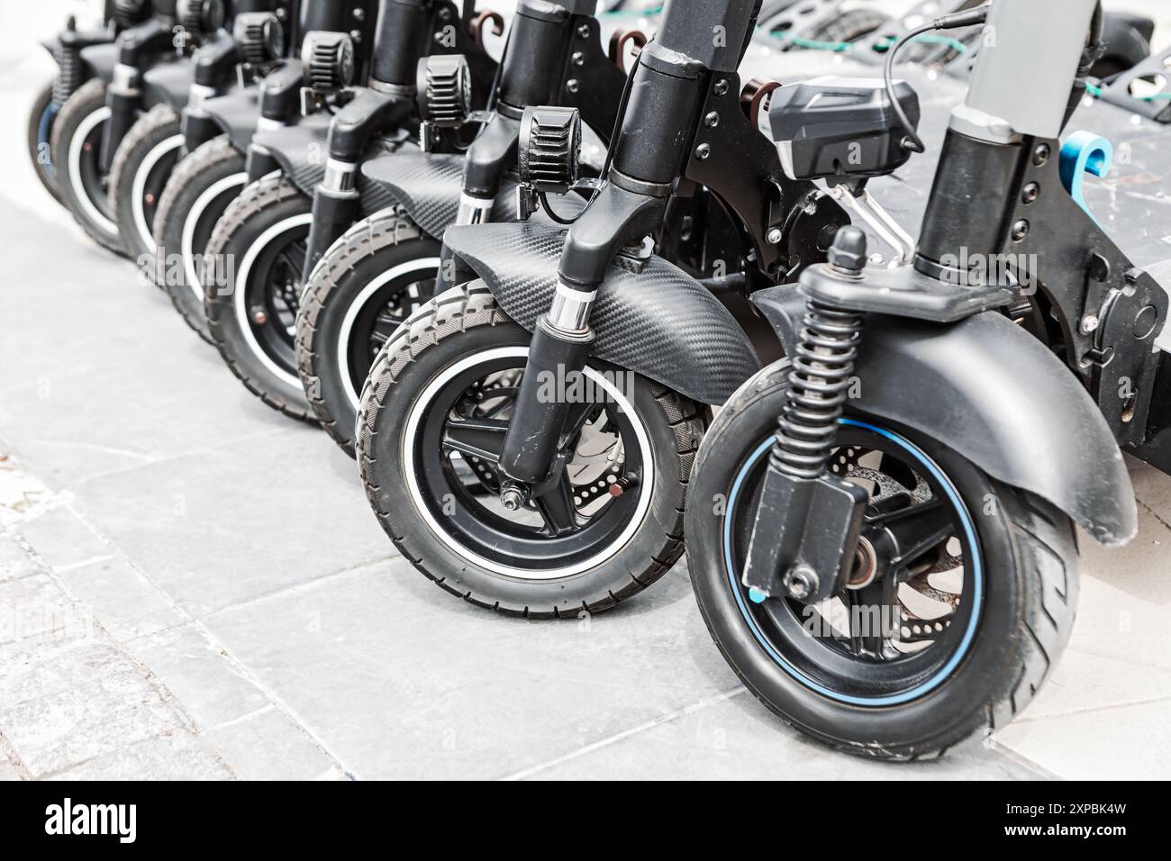 Gli scooter parcheggiavano ordinatamente in fila su un marciapiede della città. Fila di scooter elettrici a noleggio neri allineati su una strada Foto Stock