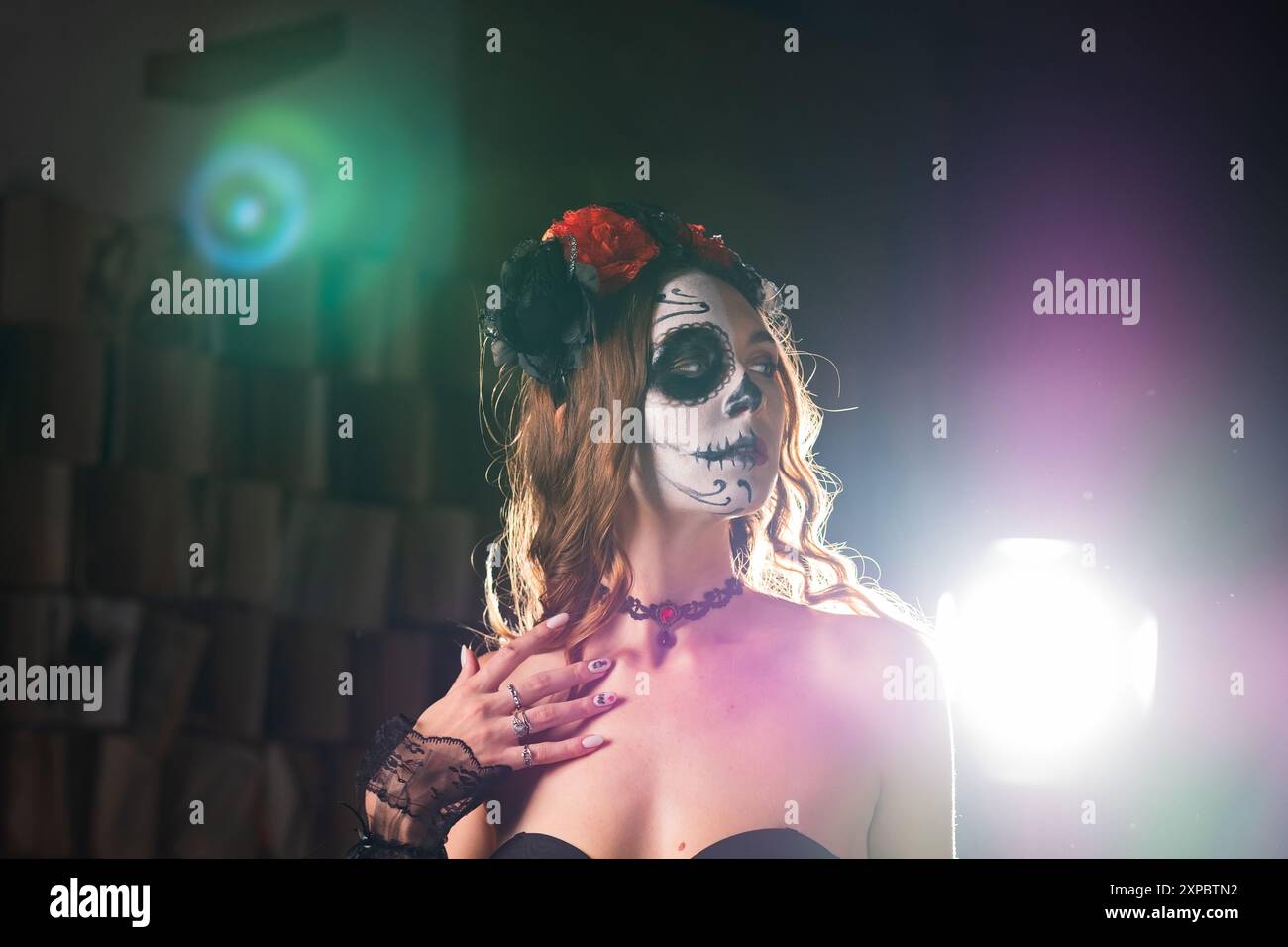 Donna adornata in un costume Day of the Dead con dettagli sul viso e corona floreale, evidenziata da una spettacolare illuminazione da studio. Foto Stock