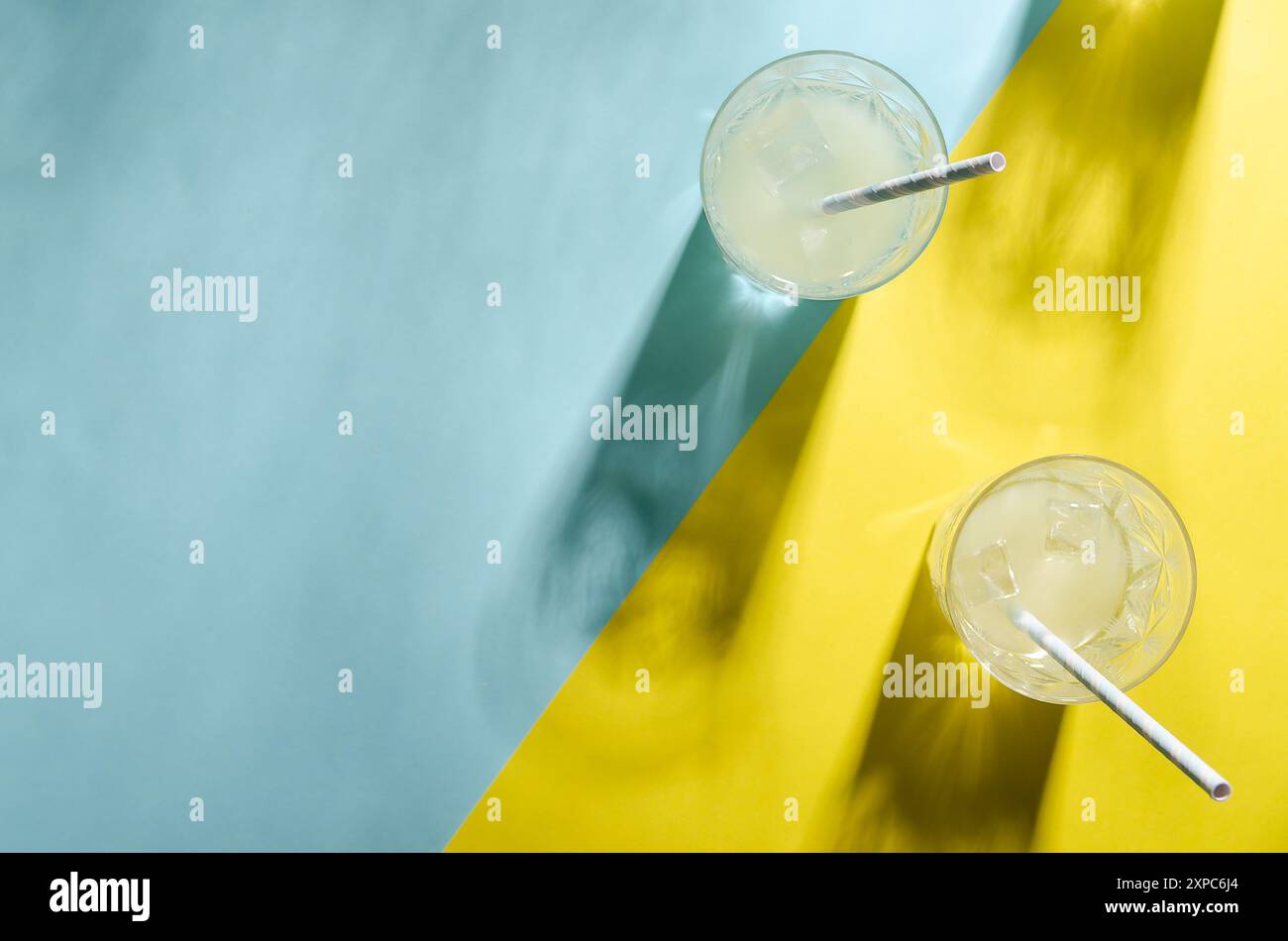 Due bicchieri di limonata con una paglia e l'ombra di un altro vetro su sfondo azzurro e giallo con spazio di copia. Foto Stock