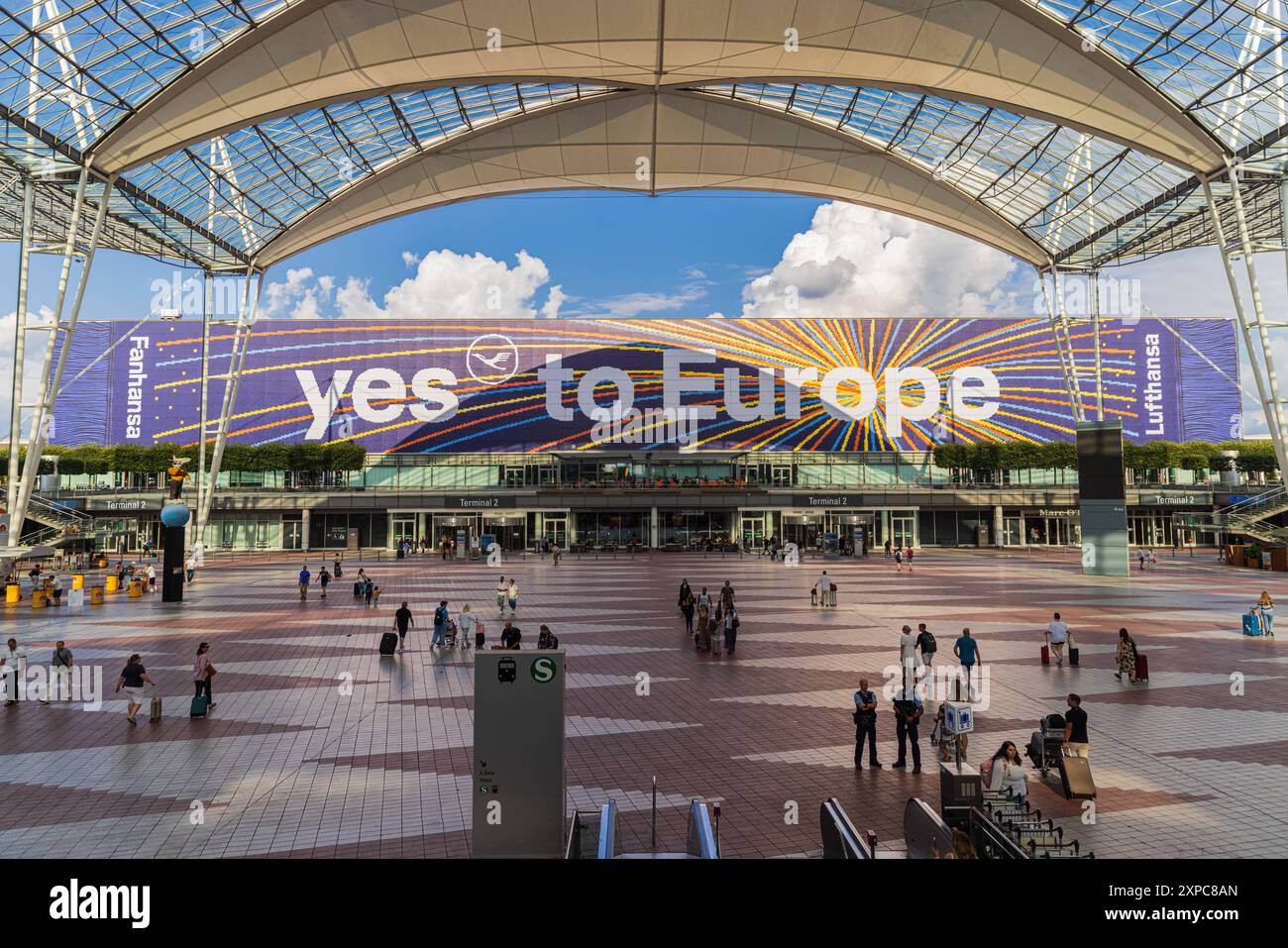 MONACO, GERMANIA - 3 AGOSTO 2024: Vista esterna dell'aeroporto di Monaco con i passeggeri sullo sfondo. Collegamento suqare tra i Terminal 1 e 2 con l Foto Stock