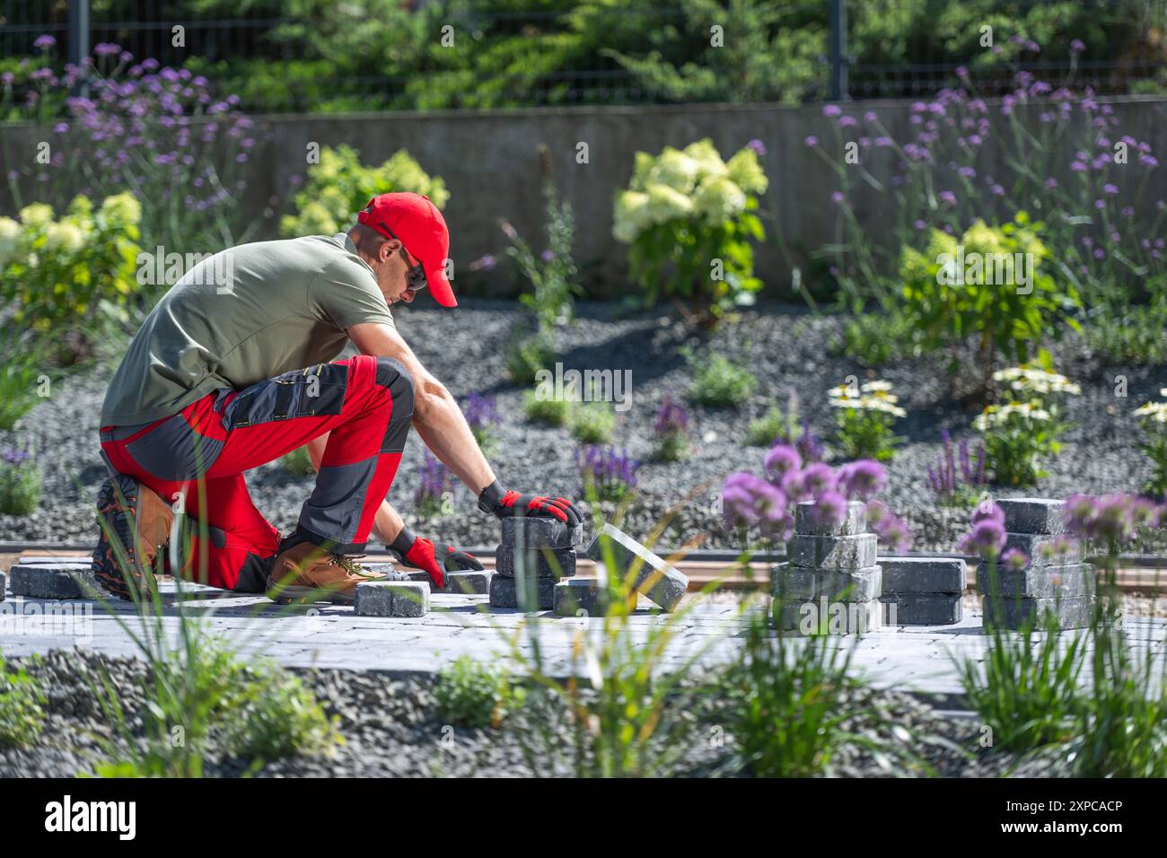 Un giardiniere organizza con cura le pietre per creare un percorso tra fiori vivaci in una giornata luminosa. Foto Stock