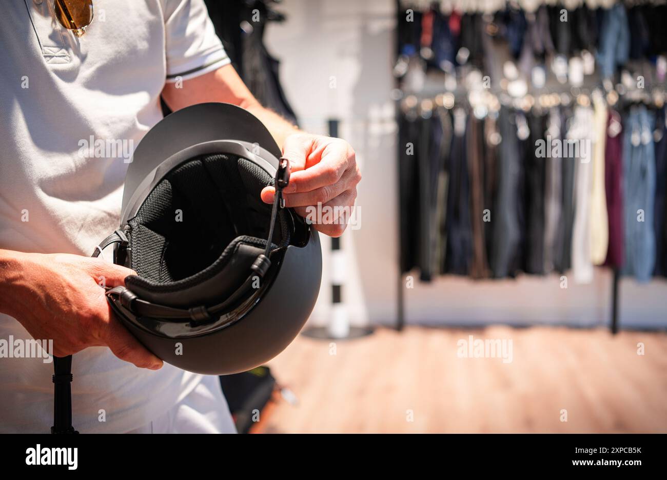 Una persona indossa un casco da equitazione all'interno di un negozio al dettaglio pieno di vari articoli di abbigliamento. Foto Stock