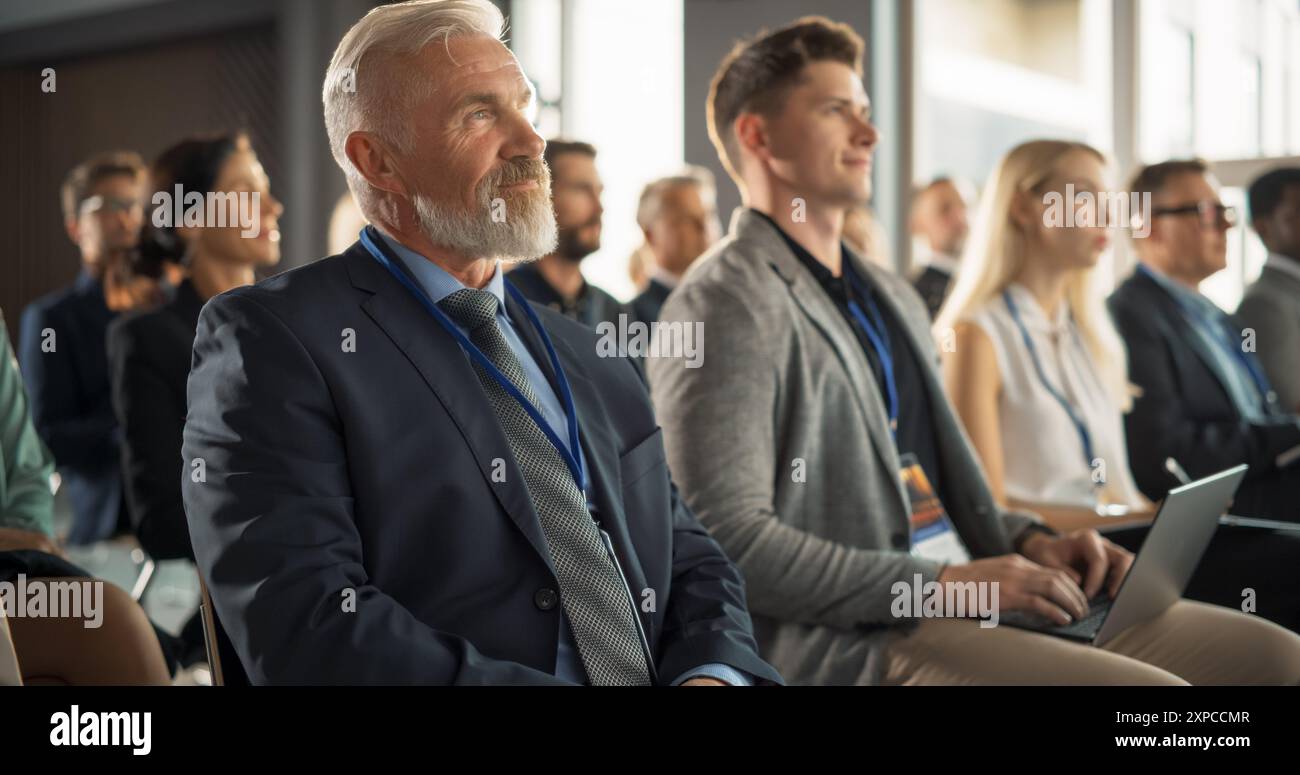 Imprenditore maschile caucasico seduto in una folla diversificata nel Business Forum. Investitore di successo che ascolta il presentatore che lancia un'idea di avvio sul palco. Uomo d'affari che partecipa alla Technology Conference. Foto Stock