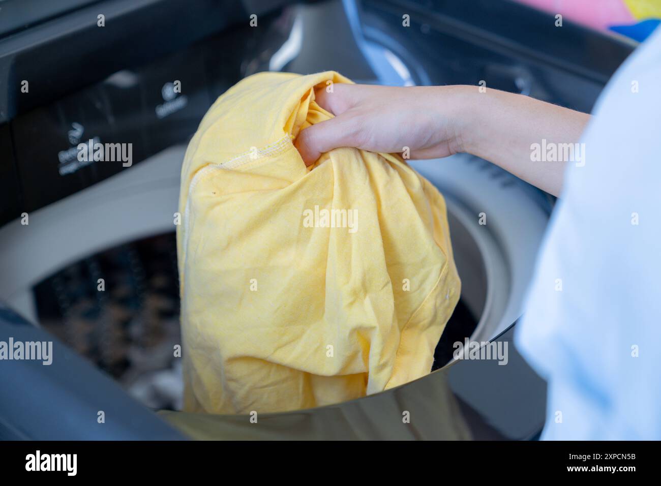 Una giovane donna sta mettendo i vestiti in una lavatrice Foto Stock