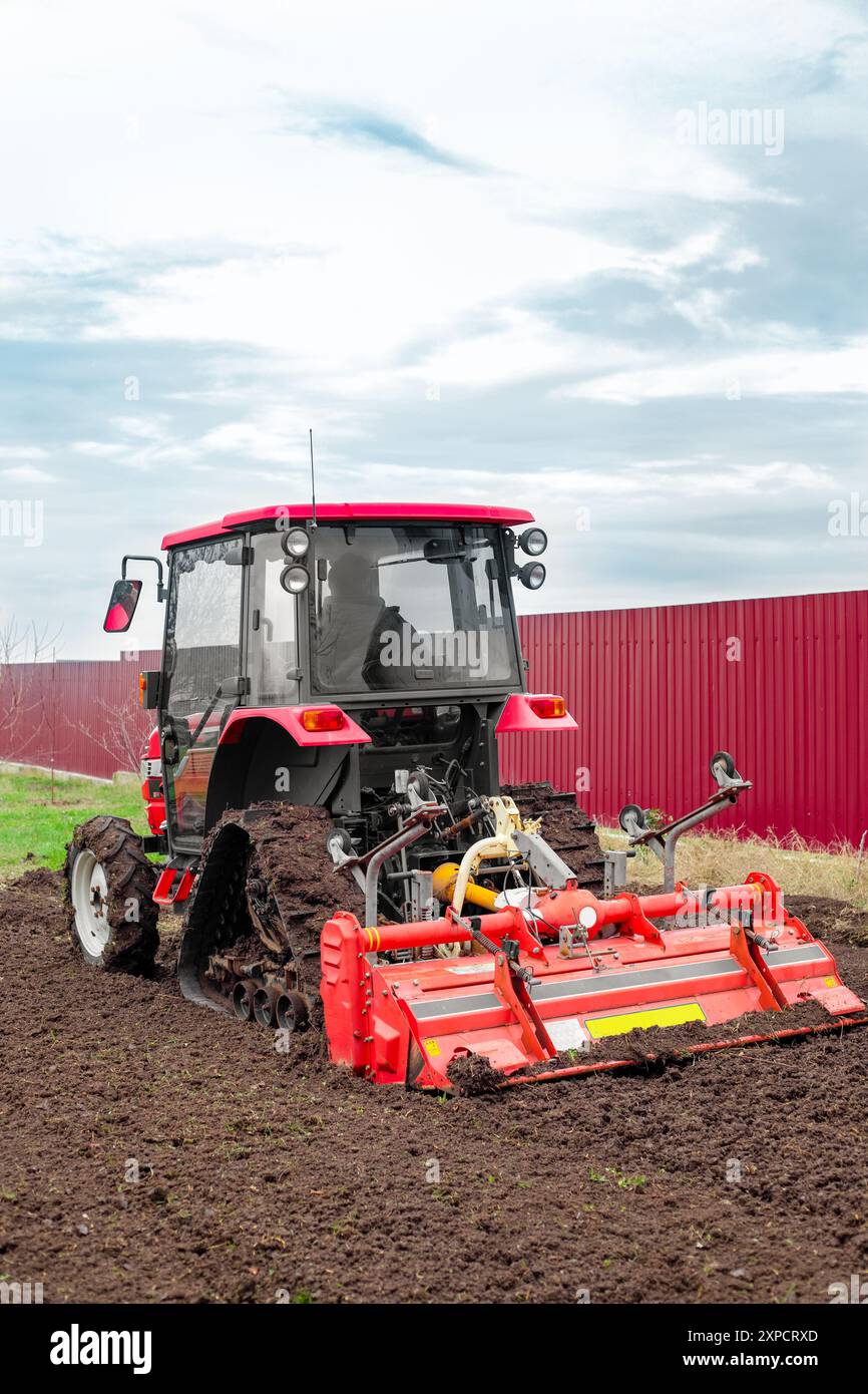 Un mini trattore con una fresatrice ara il terreno in un campo agricolo in autunno. Foto Stock