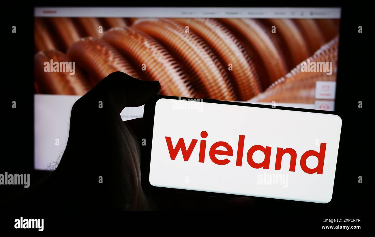 Persona che detiene un telefono cellulare con il logo della società tedesca di lavorazione dei metalli Wieland-Werke AG davanti alla pagina web aziendale. Mettere a fuoco il display del telefono. Foto Stock
