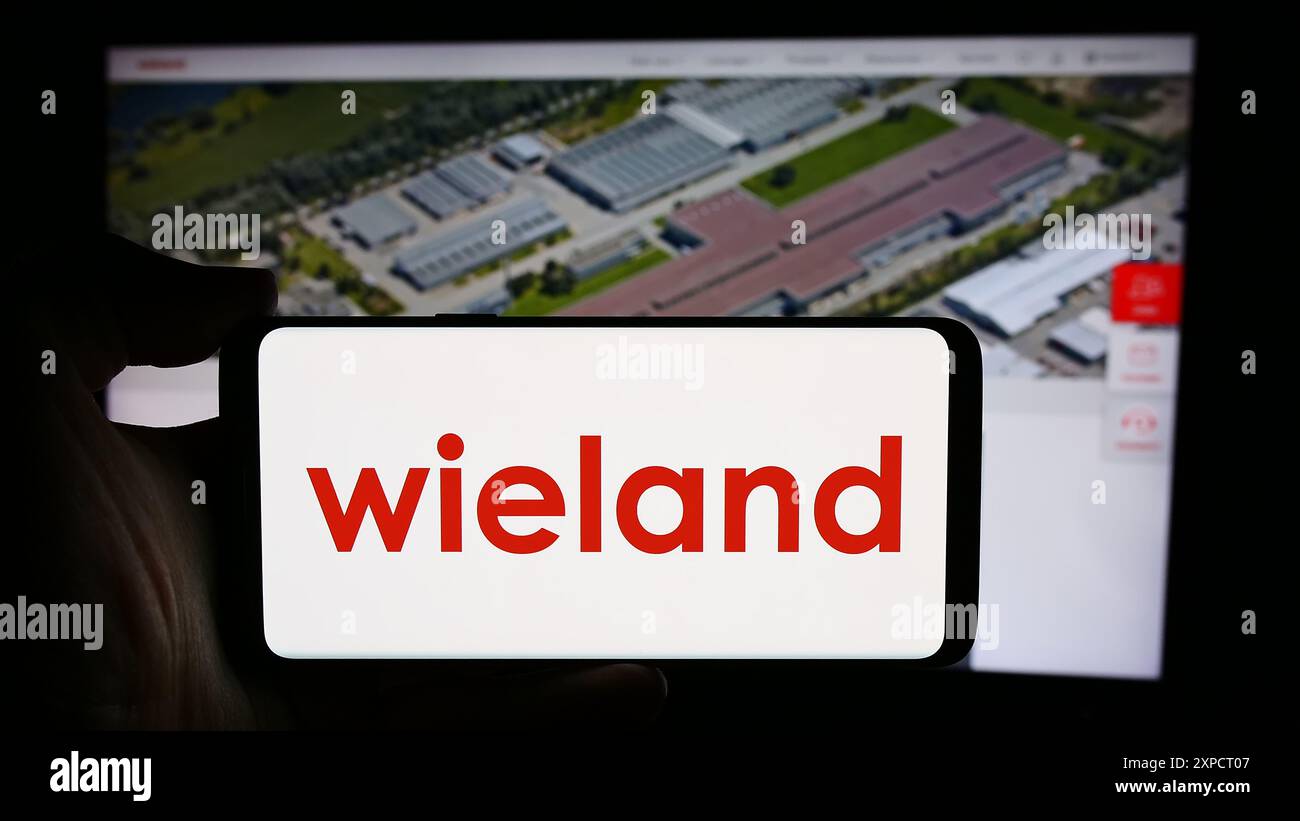 Persona che detiene un cellulare con il logo della società tedesca di lavorazione dei metalli Wieland-Werke AG davanti alla pagina web aziendale. Mettere a fuoco il display del telefono. Foto Stock