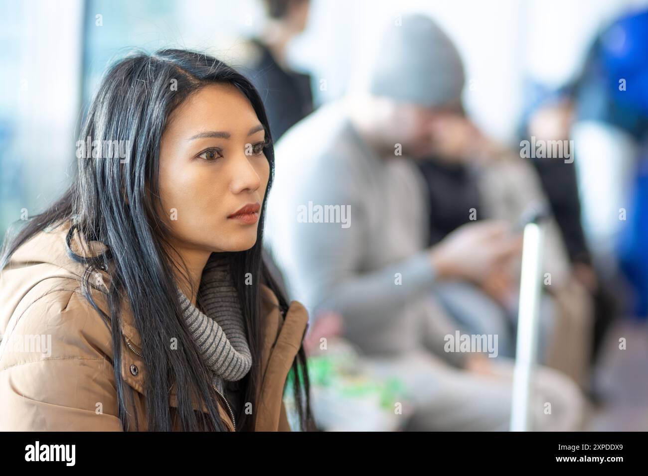 Una giovane donna con un cappotto è seduta in sala d'attesa Foto Stock