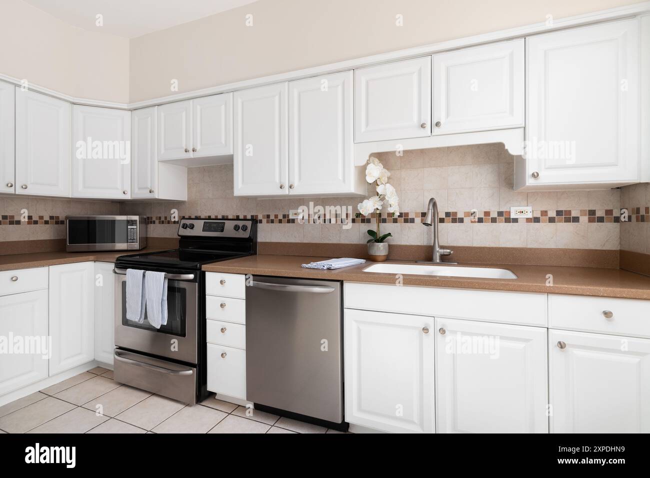 Una cucina con armadi bianchi, armadi al quarzo marrone e un backsplash con piastrelle marroni a mosaico. Nessun marchio o etichetta. Foto Stock