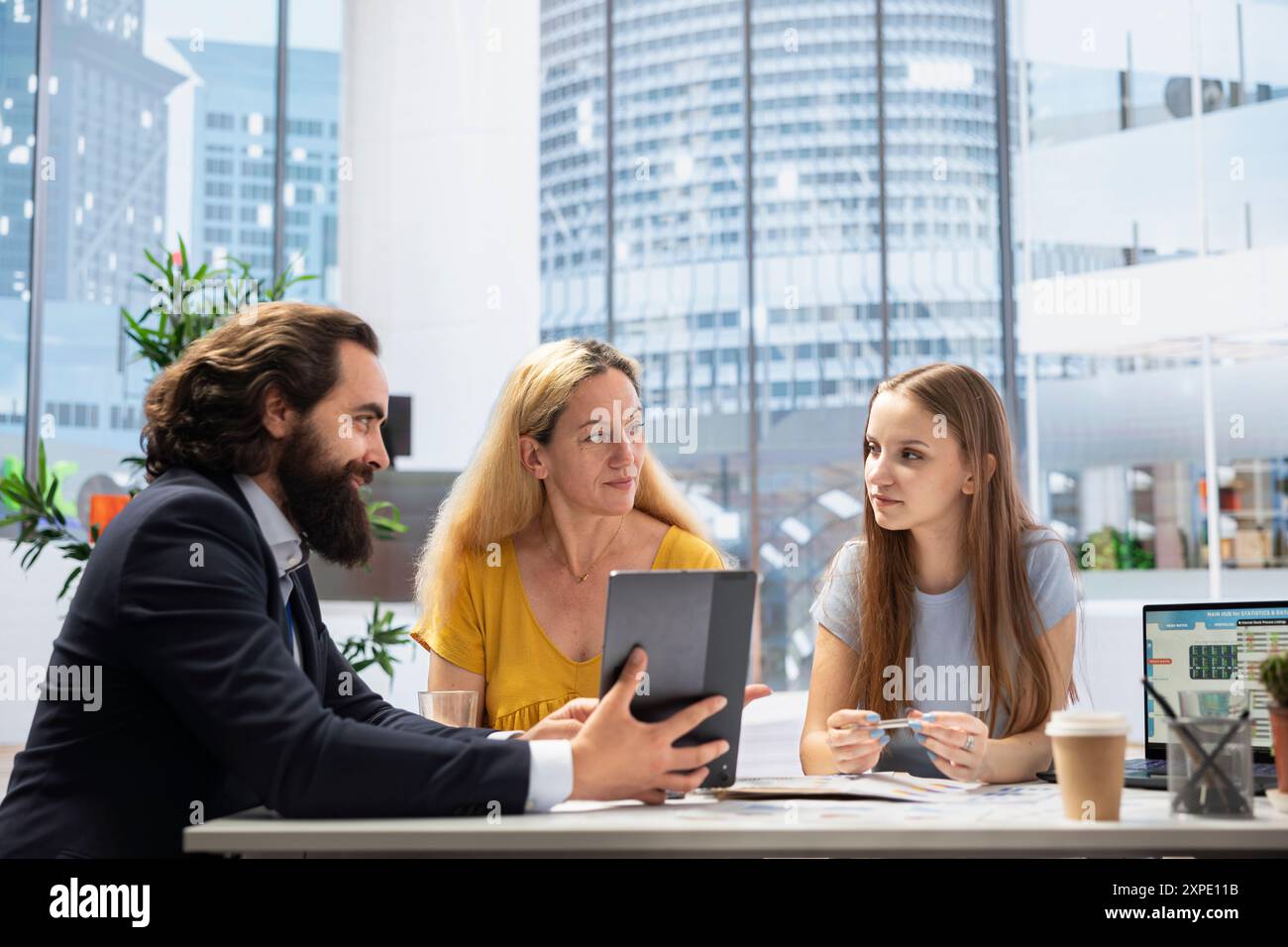 Il consulente finanziario utilizza il software su tablet per calcolare il patrimonio netto dei clienti, prendendo in considerazione attività e passività. L'agente in riunione d'ufficio utilizza il dispositivo per aiutare la famiglia a decidere quanto denaro investire Foto Stock