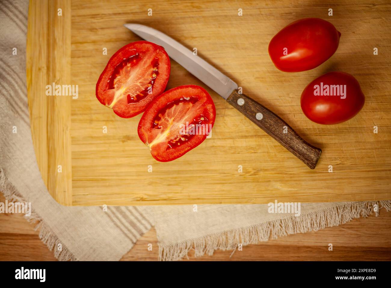 Pomodori rossi succosi biologici e un coltello con manico in legno su un tagliere rustico con un tovagliolo di lino. Foto Stock