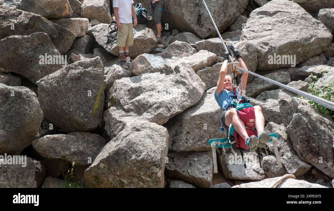 Una donna adulta che attraversa una traversata tirolese sospesa sopra Boulder Creek nel Boulder Canyon, Boulder, Colorado Foto Stock