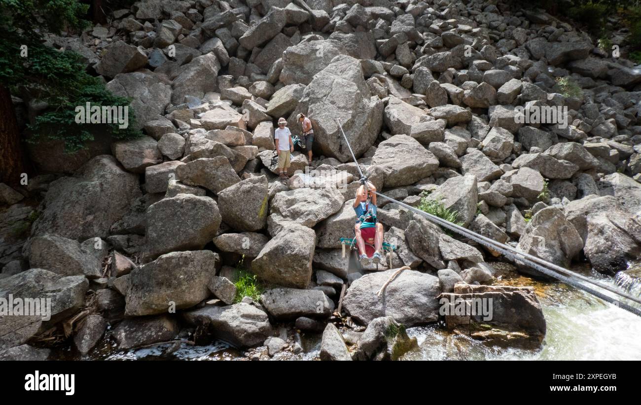 Una donna adulta che attraversa una traversata tirolese sospesa sopra Boulder Creek nel Boulder Canyon, Boulder, Colorado Foto Stock