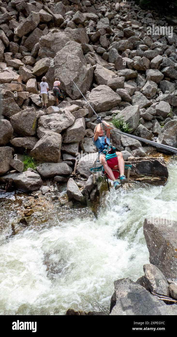 Una donna adulta che attraversa una traversata tirolese sospesa sopra Boulder Creek nel Boulder Canyon, Boulder, Colorado Foto Stock