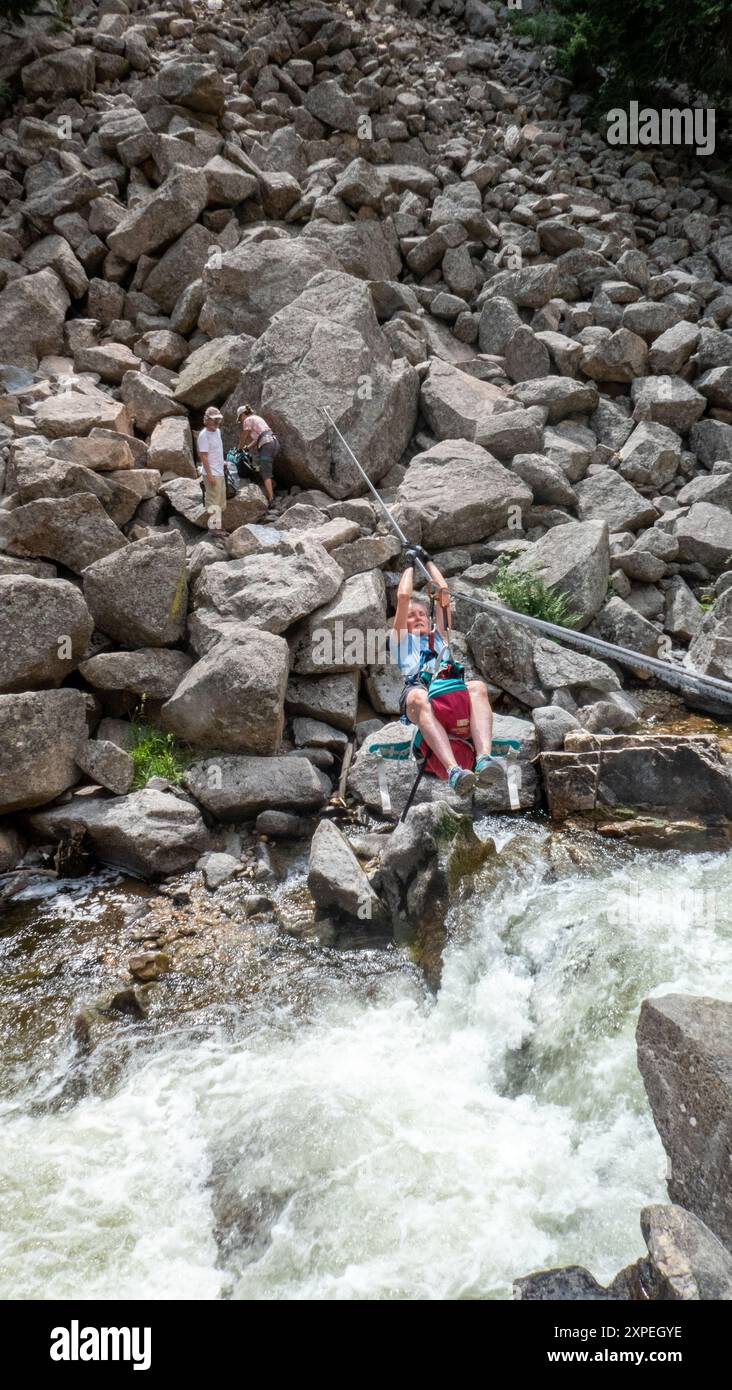 Una donna adulta che attraversa una traversata tirolese sospesa sopra Boulder Creek nel Boulder Canyon, Boulder, Colorado Foto Stock