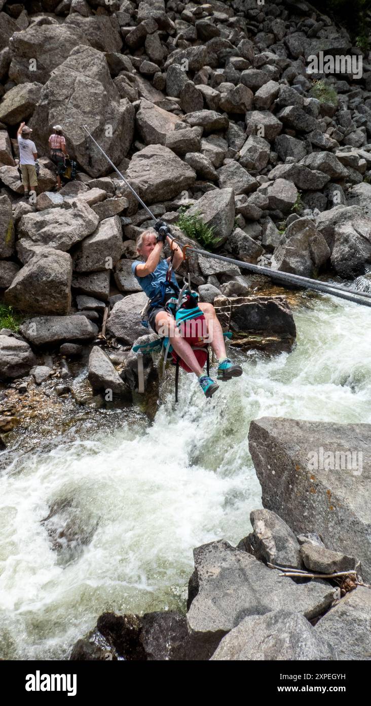 Una donna adulta che attraversa una traversata tirolese sospesa sopra Boulder Creek nel Boulder Canyon, Boulder, Colorado Foto Stock