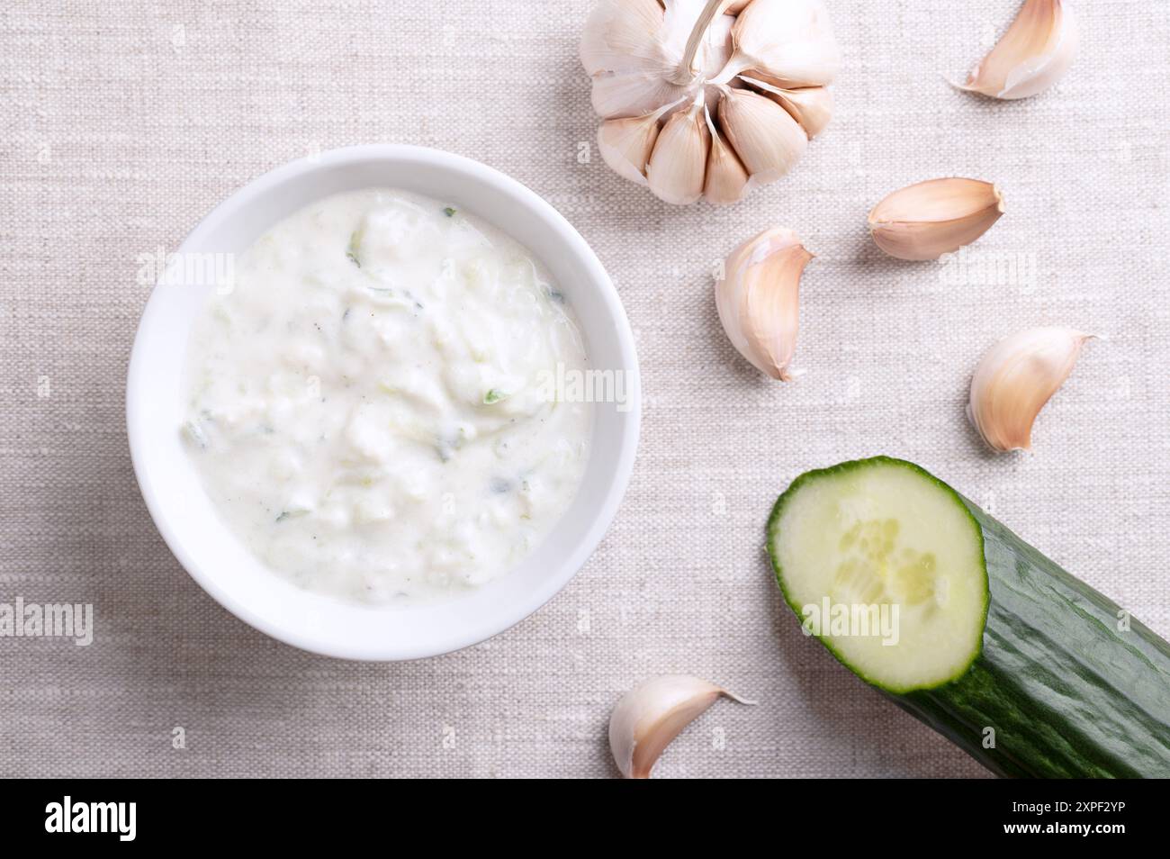 Tzatziki fresco in una ciotola bianca su tessuto di lino. Salsa rinfrescante, zuppa o salsa, fatta di yogurt affaticato salato, mescolato con cetrioli, aglio ed erbe aromatiche. Foto Stock