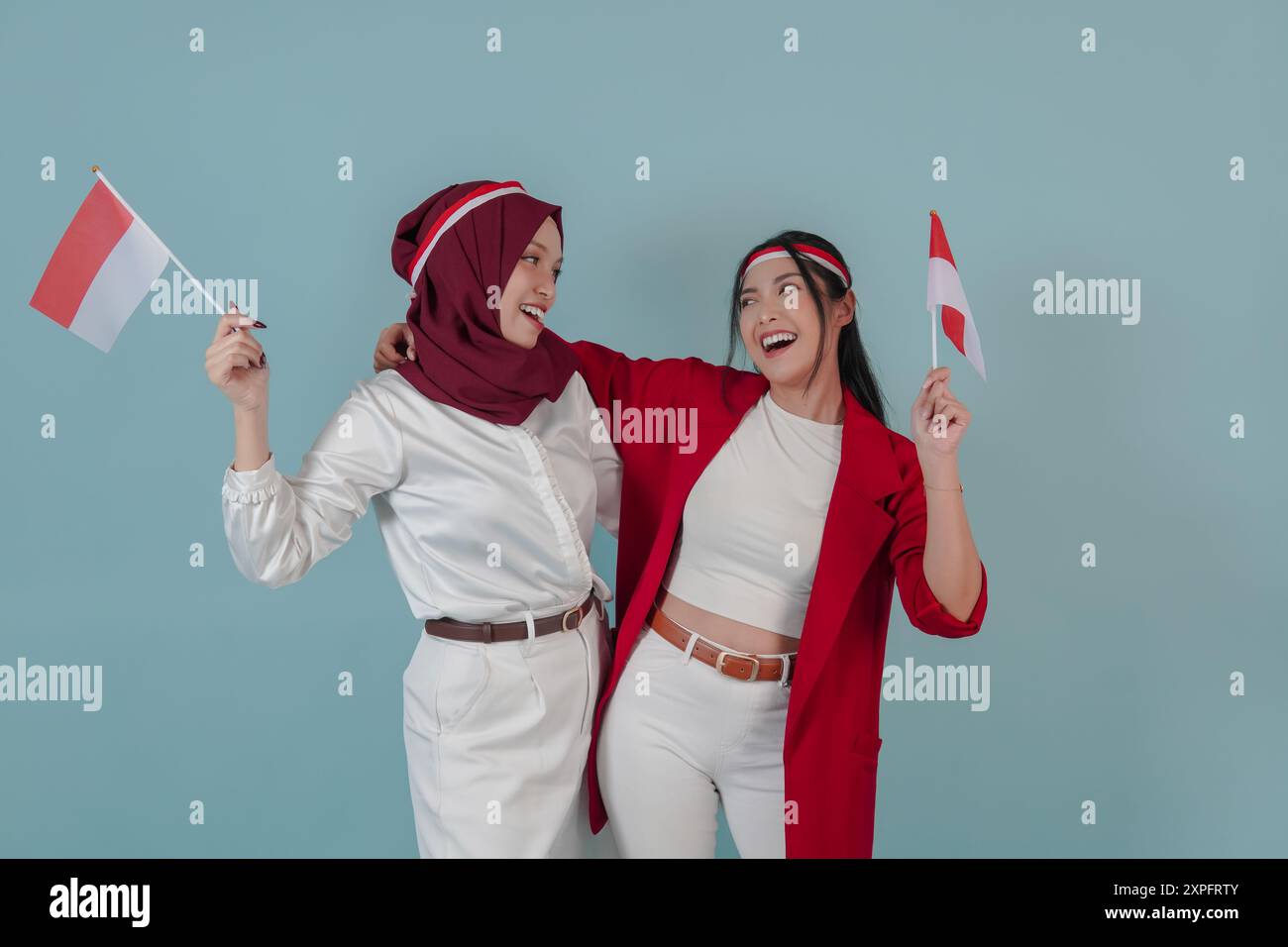 Due belle donne indonesiane che tengono una mini bandiera mentre si guardano l'un l'altra con un sorriso. Indonesia Independence Day Concept. Foto Stock