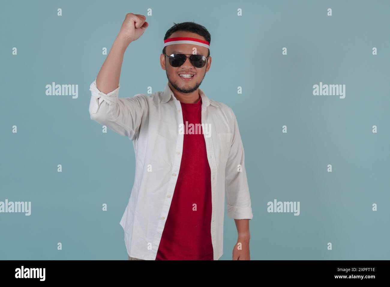 Bel giovane asiatico con gli occhiali da sole sta alzando le mani in aria con un'espressione felice. Indonesia Independence Day Concept. Foto Stock