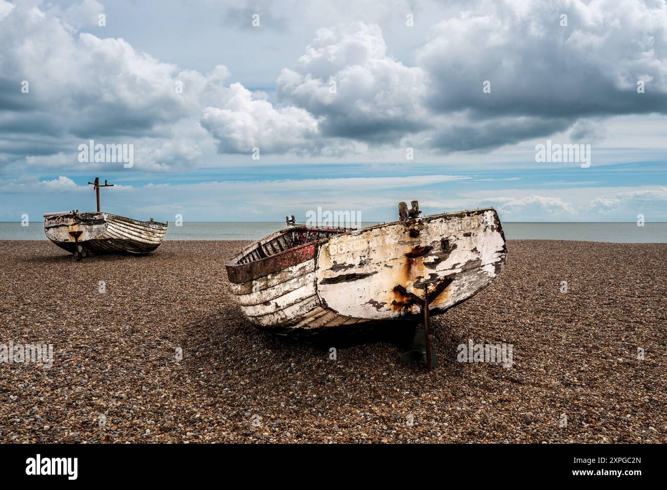 Due vecchie barche da pesca costiere con scafo in legno terminano i loro giorni sulla spiaggia di ciottoli di Aldeburgh, Suffolk. Vista sulla costa. Cielo nuvoloso. Foto Stock