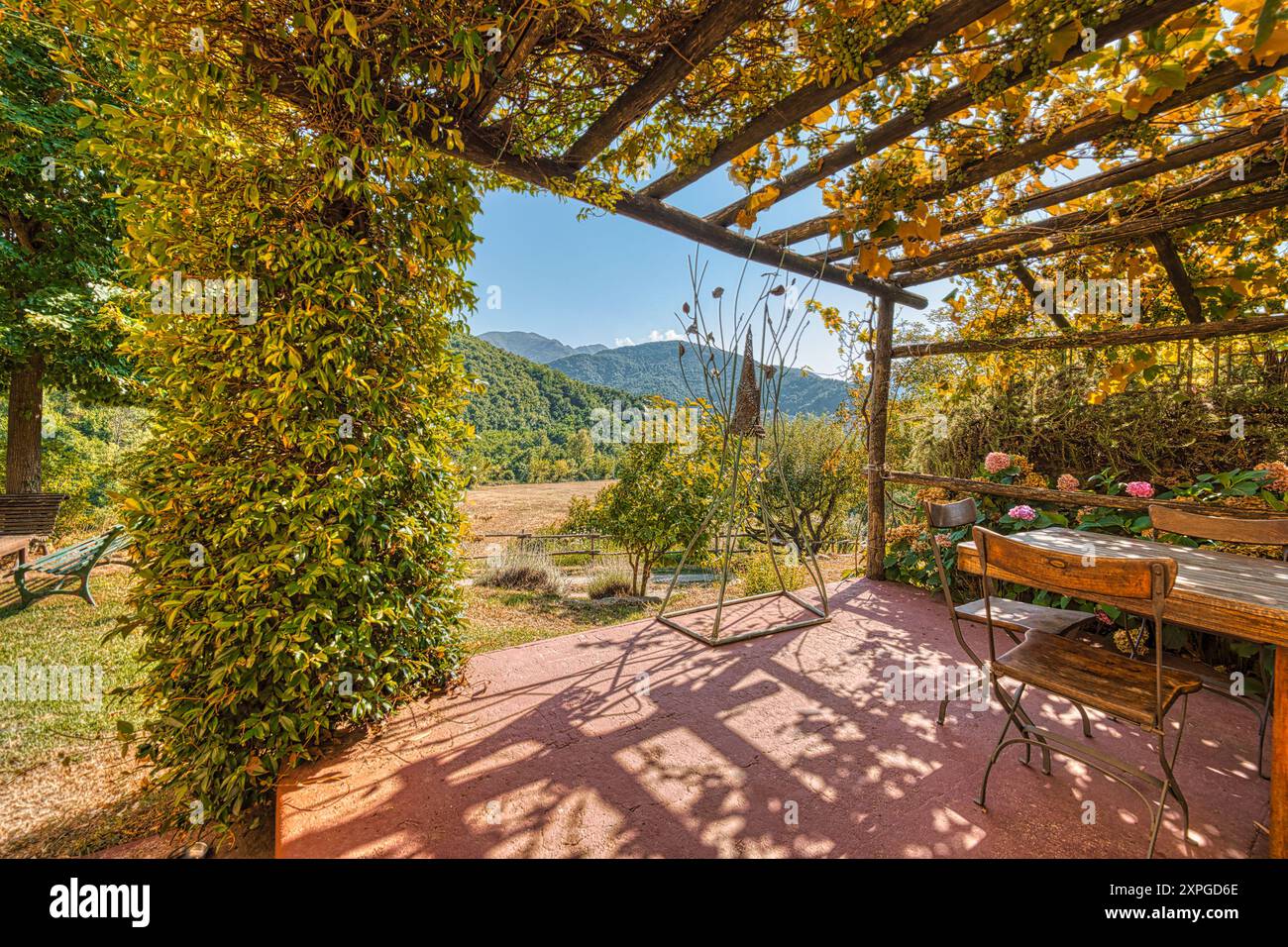 Una tranquilla fuga in campagna: Un affascinante pergolato adornato da vegetazione lussureggiante e fiori vibranti, sullo sfondo di dolci colline Foto Stock