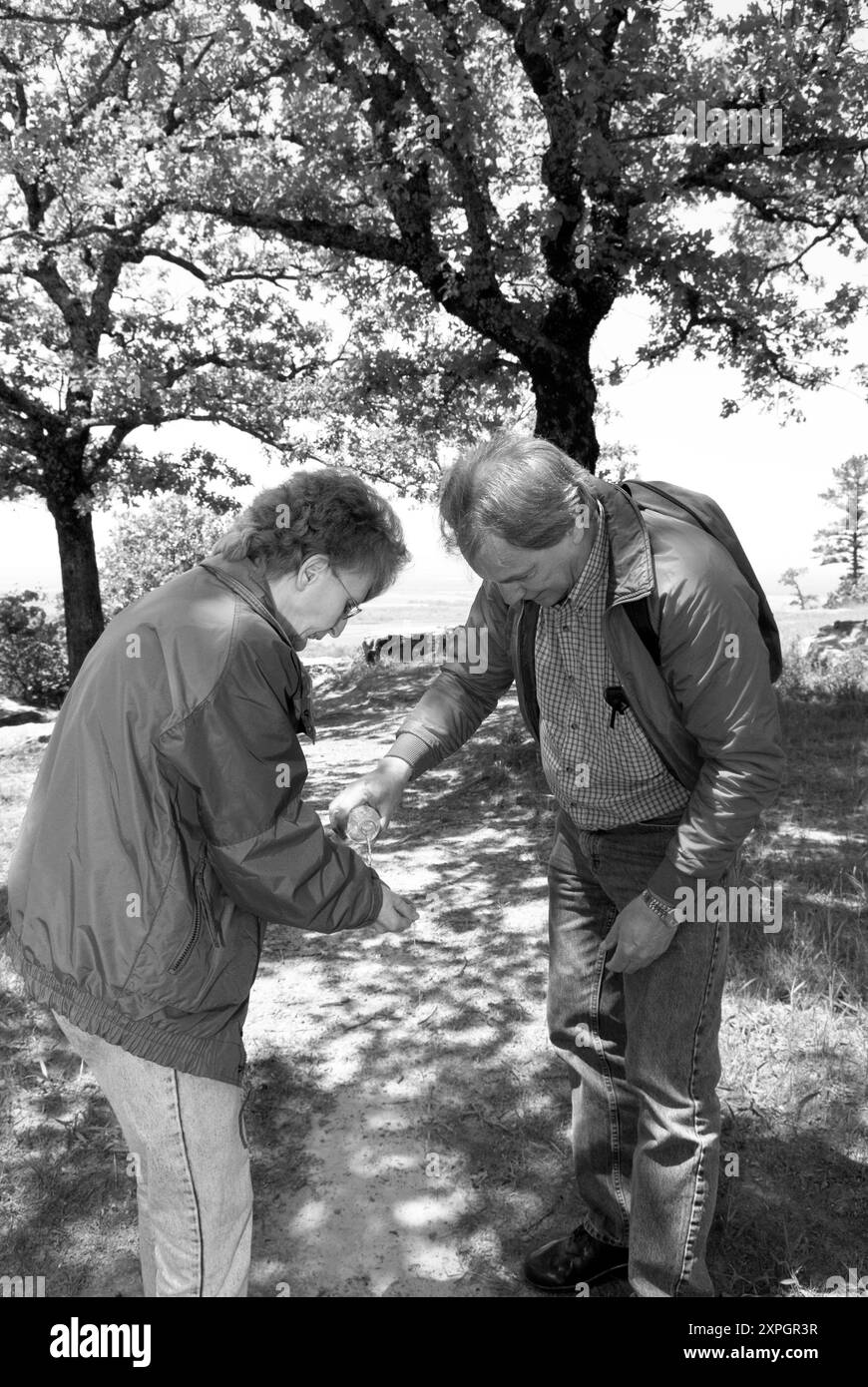 Donna caucasica da 50 a 55 anni si lava le mani con acqua in bottiglia versata da un uomo sul sentiero del Petit Jean State Park vicino a Morrilton, Arca. STATI UNITI Foto Stock
