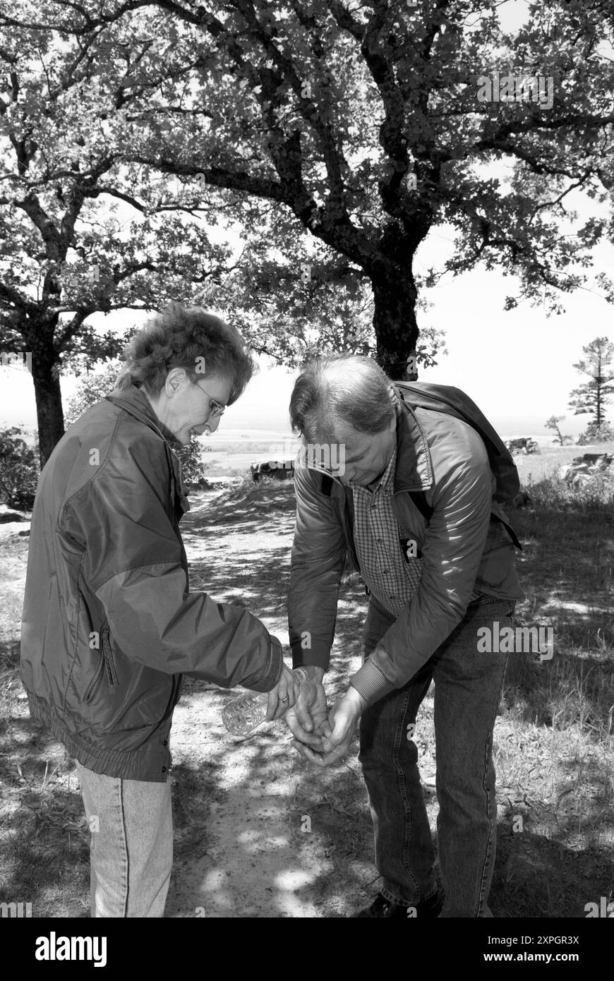 Maschio caucasico di età compresa tra i 50 e i 55 anni lavandosi le mani con acqua in bottiglia versata da una femmina sul sentiero del Petit Jean State Park, vicino a Morrilton, Arkansas. Foto Stock