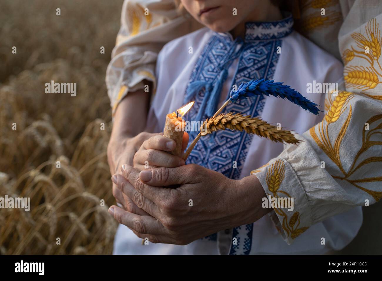 Candela in fiamme e due orecchie di grano, dipinte in colori giallo-blu nelle mani di madre e figlio ucraini tra i campi di grano. Spikelet e fuoco a memor Foto Stock