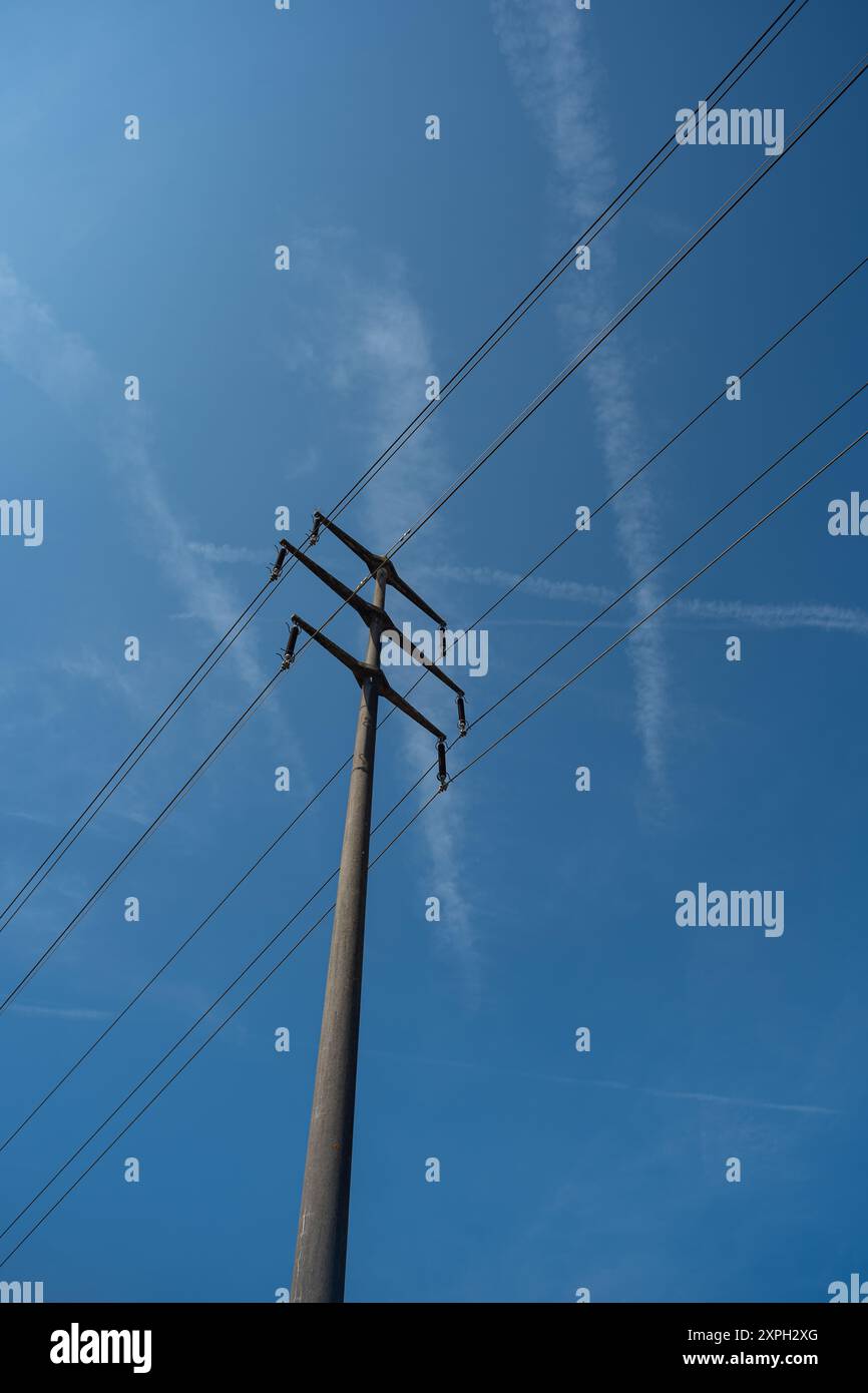 Polo della linea di alimentazione ad alta tensione in un campo. Spettacolo con angolazioni basse, cielo blu sullo sfondo, nessuna gente. Foto Stock