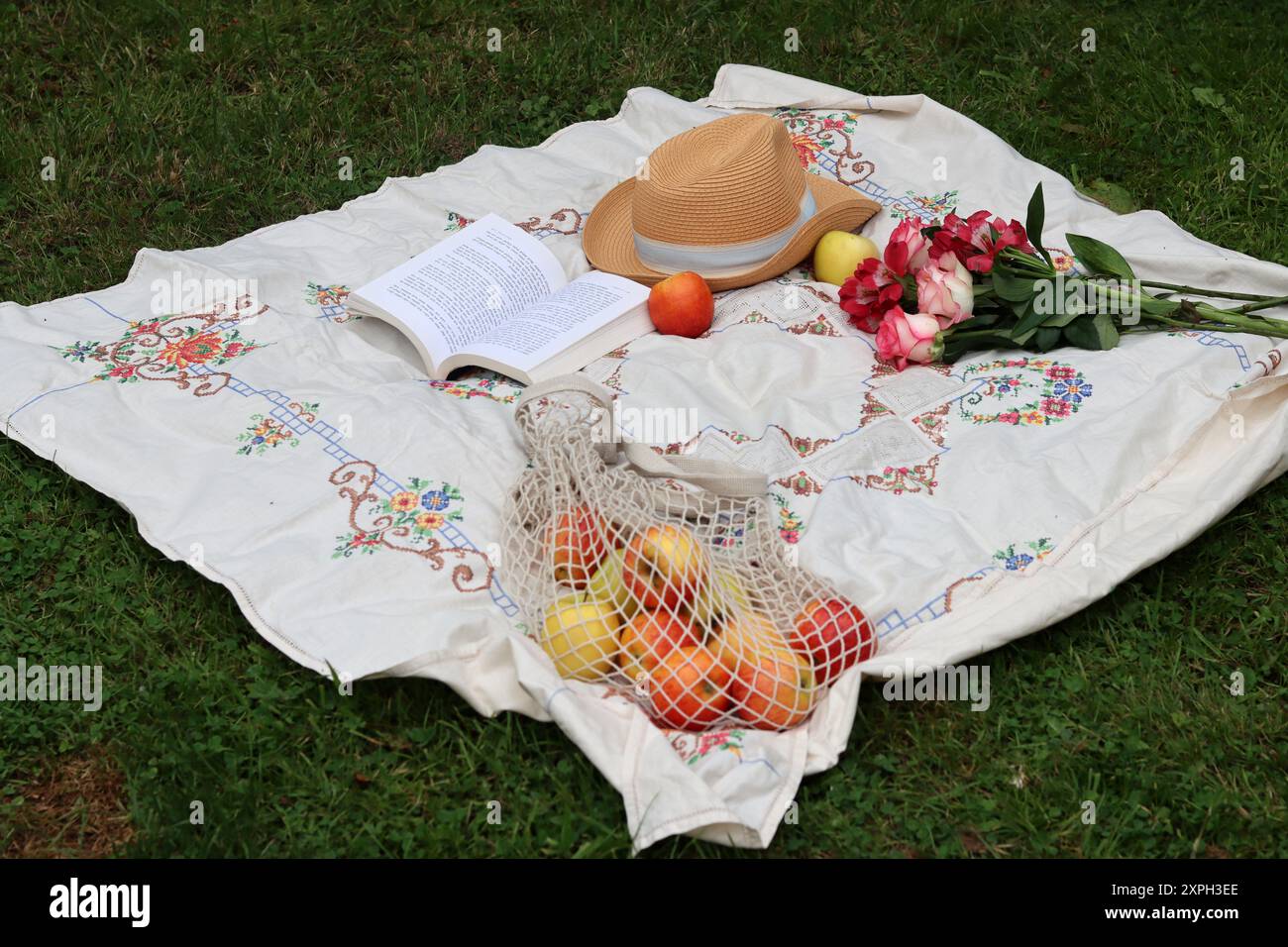 Bouquet di rose, mele, libro aperto e cappello di paglia su una coperta da picnic. Attività nel weekend estivo. Concetto di vita sana. Foto Stock