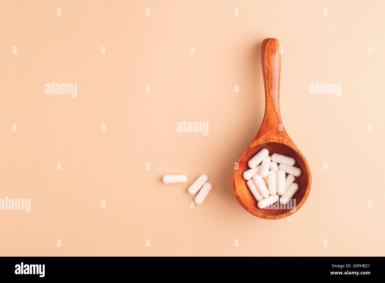 Cucchiaio di legno con capsule bianche su sfondo beige, vista dall'alto. Integratori alimentari e rimedi naturali in una composizione semplice ed elegante. Foto Stock