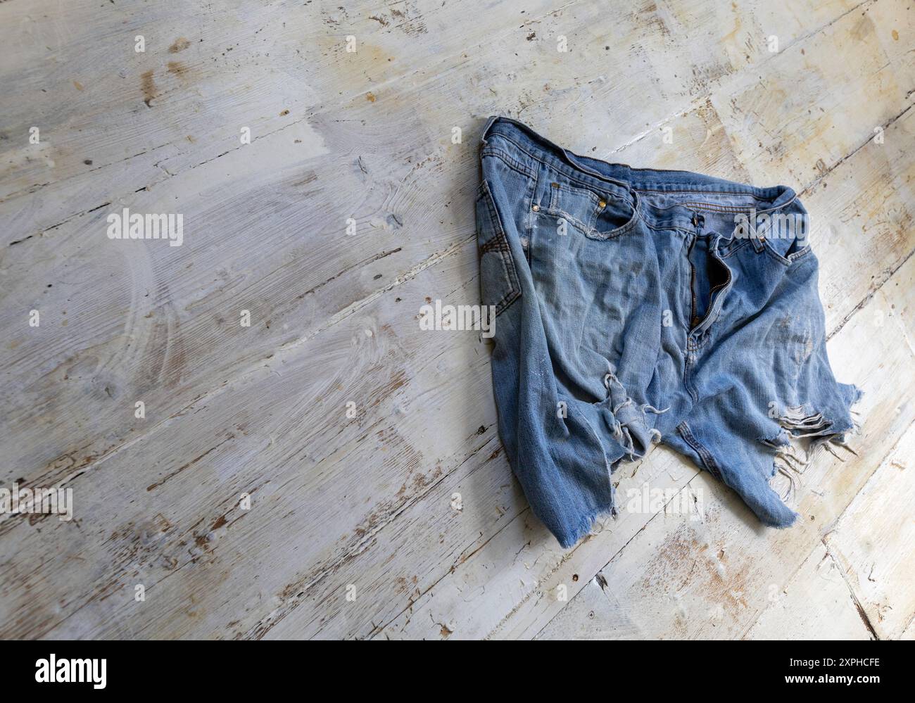 Pantaloncini in denim blu con taglio molto consumato, su tavole da pavimento lavate di bianco, con zip, sfilacciato e strappato, forse di moda per alcuni. Foto Stock