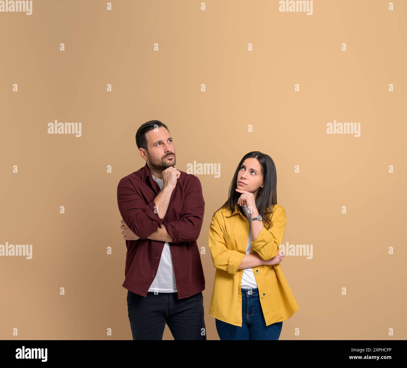 Giovane coppia incerta con le mani sul mento che pensa alla soluzione. Giovane uomo serio e donna vestito con camicie che contemplano e guardano in alto mentre sta Foto Stock