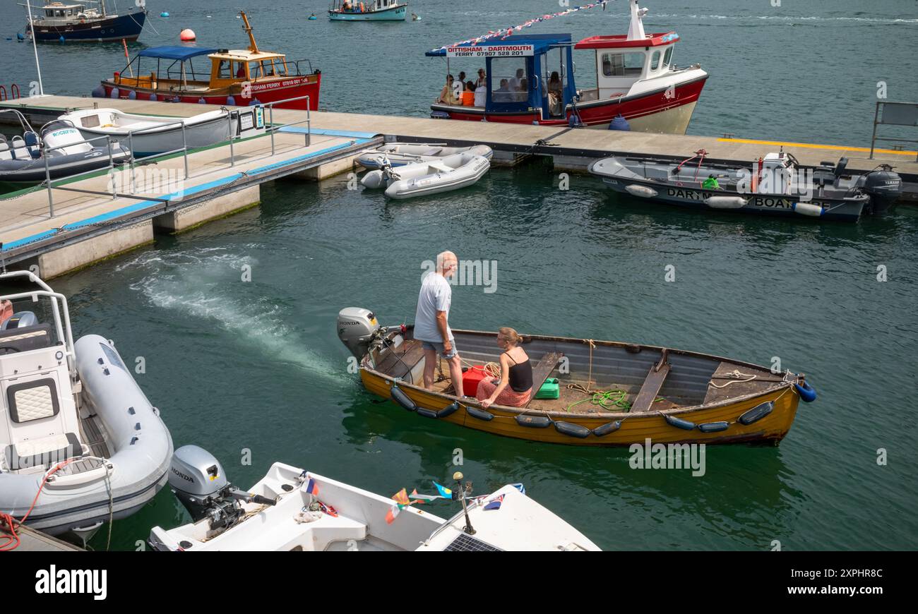 Una piccola barca di legno alimentata da un motore fuoribordo con un uomo e una donna che passano davanti al traghetto Dittisham a Dartmouth, Devon, Regno Unito Foto Stock