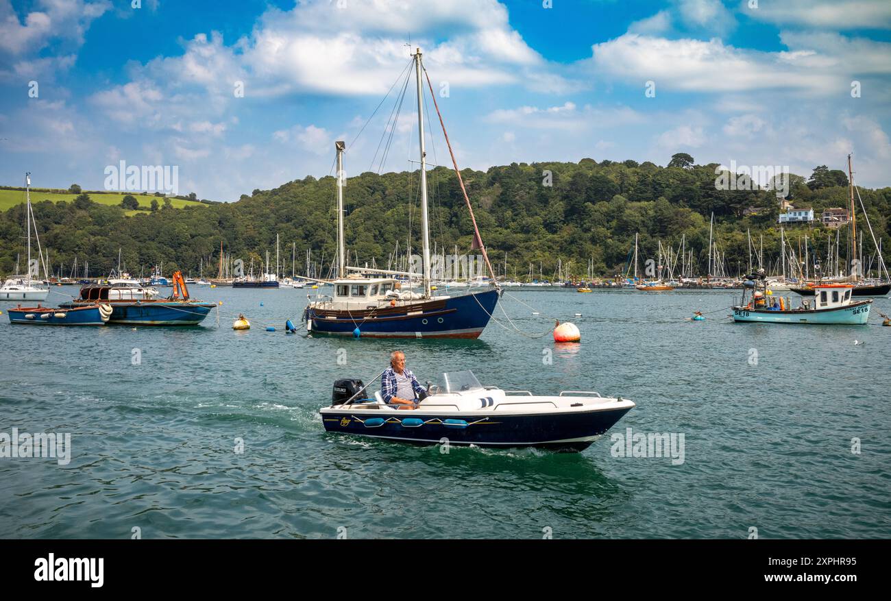 Una piccola barca alimentata da un motore fuoribordo con un uomo che passa davanti a barche ormeggiate nell'estuario del Dart, Dartmouth, Devon, Regno Unito Foto Stock