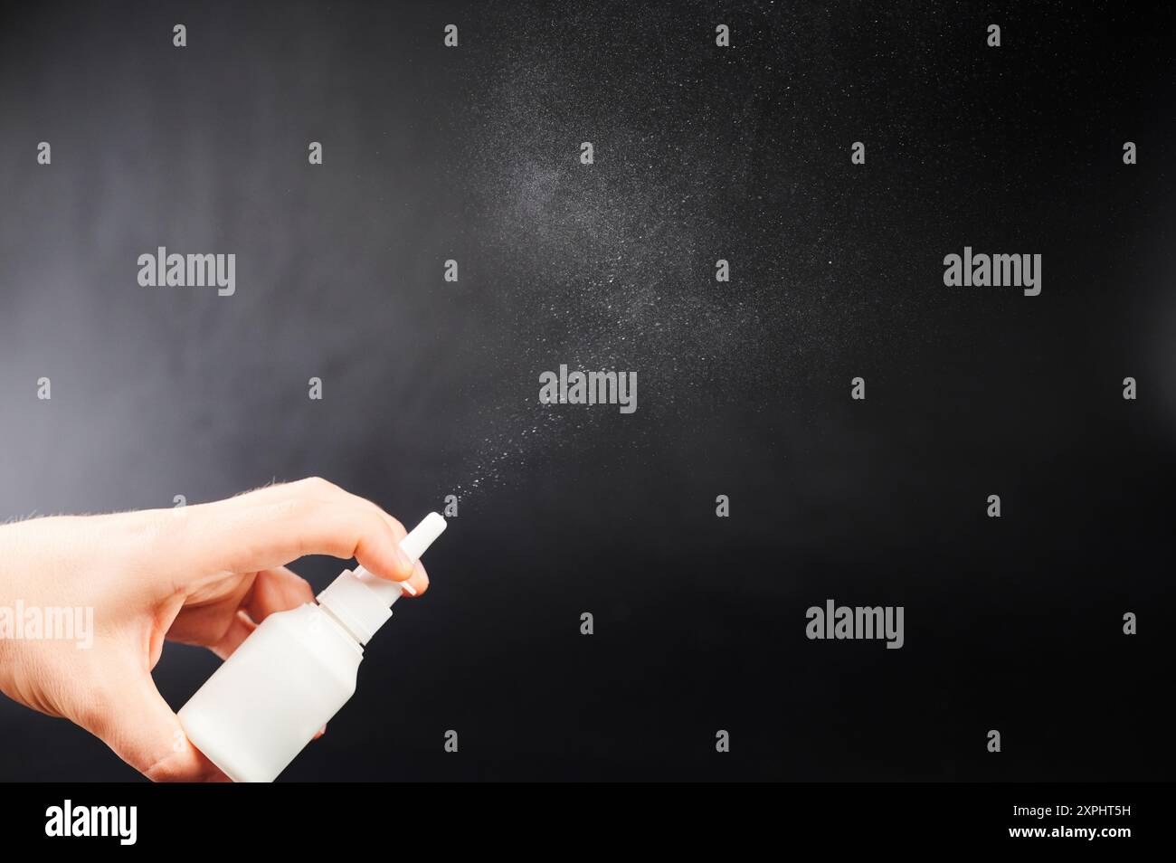Spray nasale in mano che fuoriesce dall'ugello isolato su sfondo nero studio Foto Stock