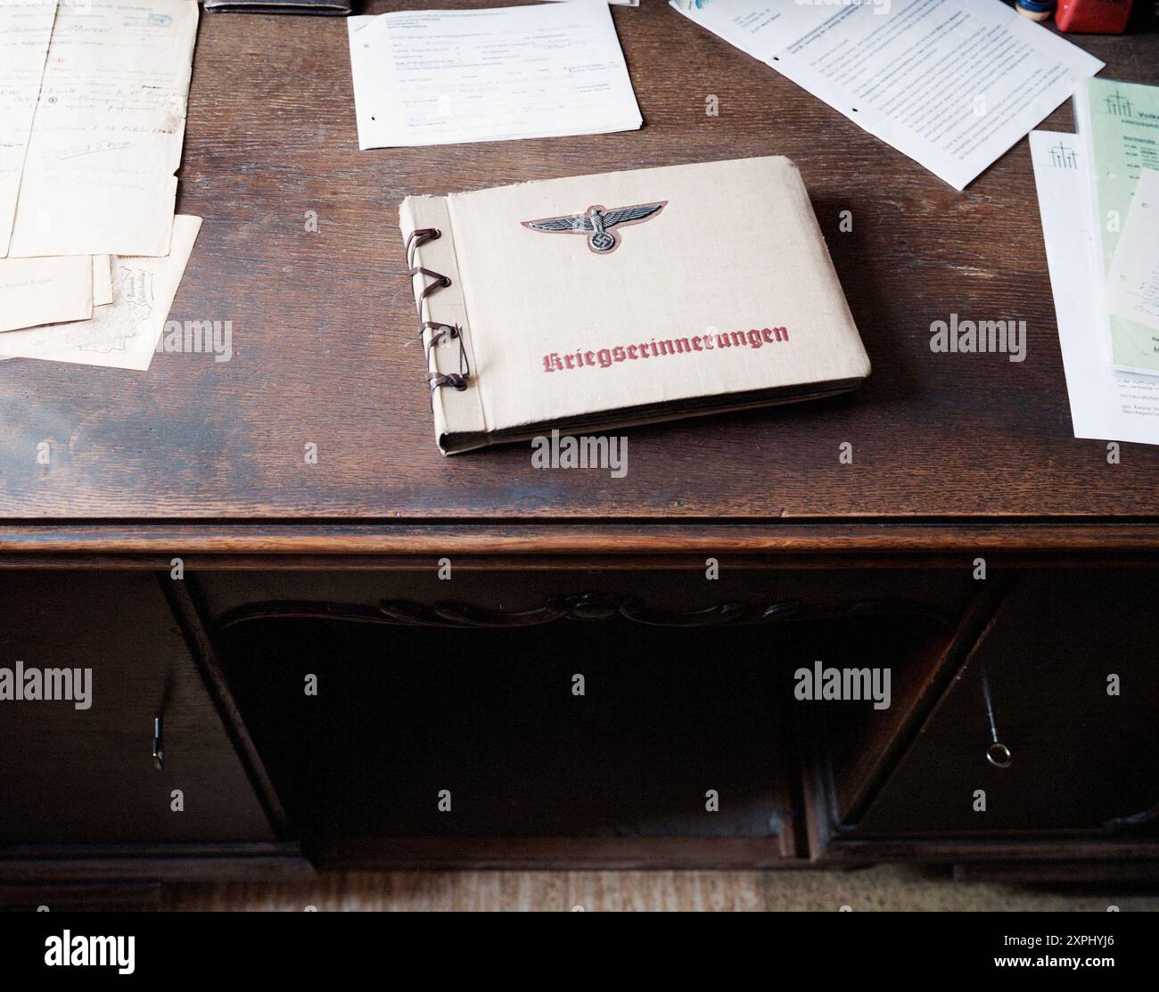 Fotografia di un libro di cimeli della seconda guerra mondiale del terzo Reich intitolato "Kriegserinnerungen" dalla Germania nazista, collocato su una scrivania di legno circondata da documenti sparsi. Rappresenta manufatti storici, memorie di guerra e storia tedesca Foto Stock