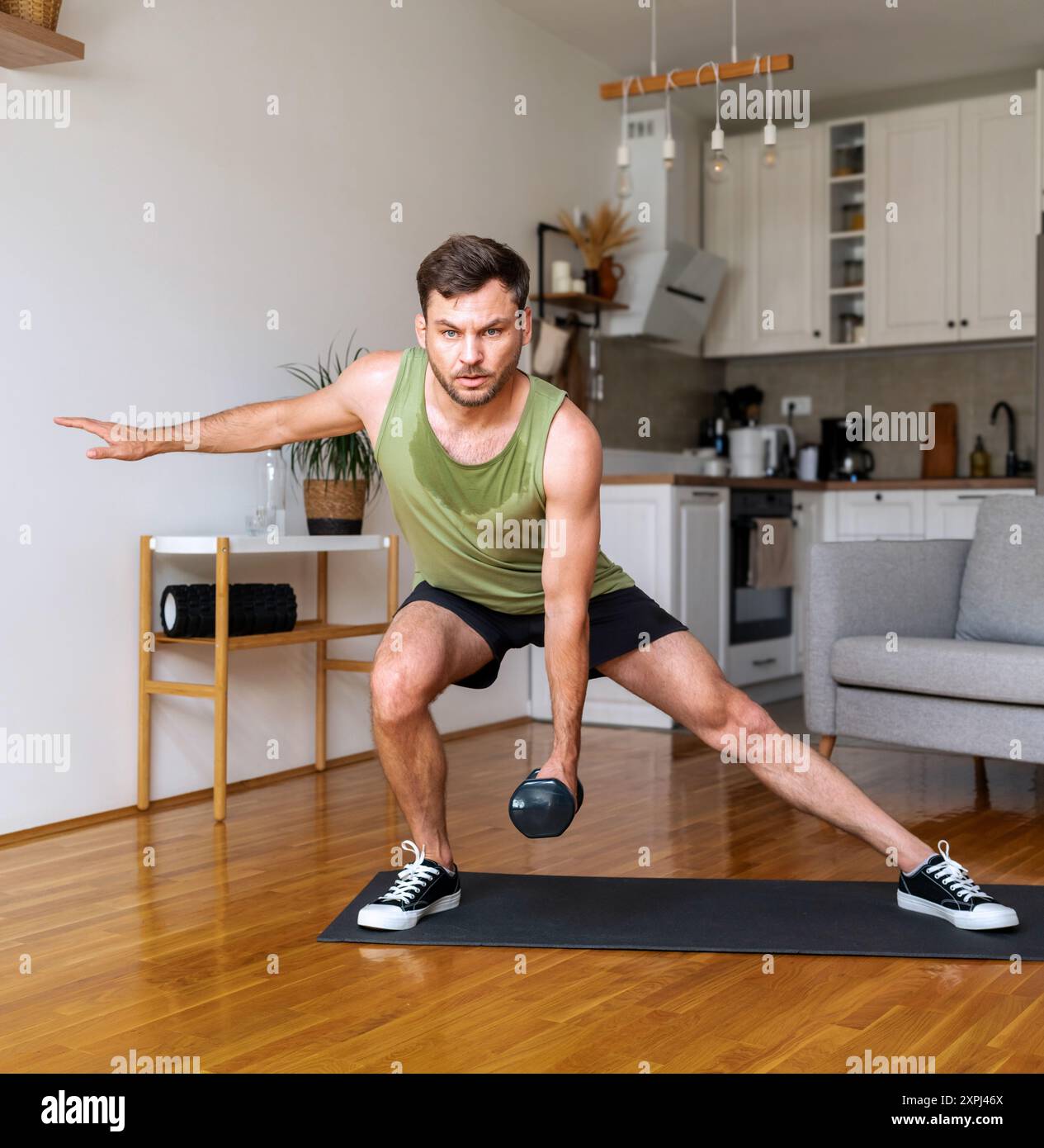 Giovane uomo adulto che fa l'allenamento a casa usando i manubri. Foto Stock