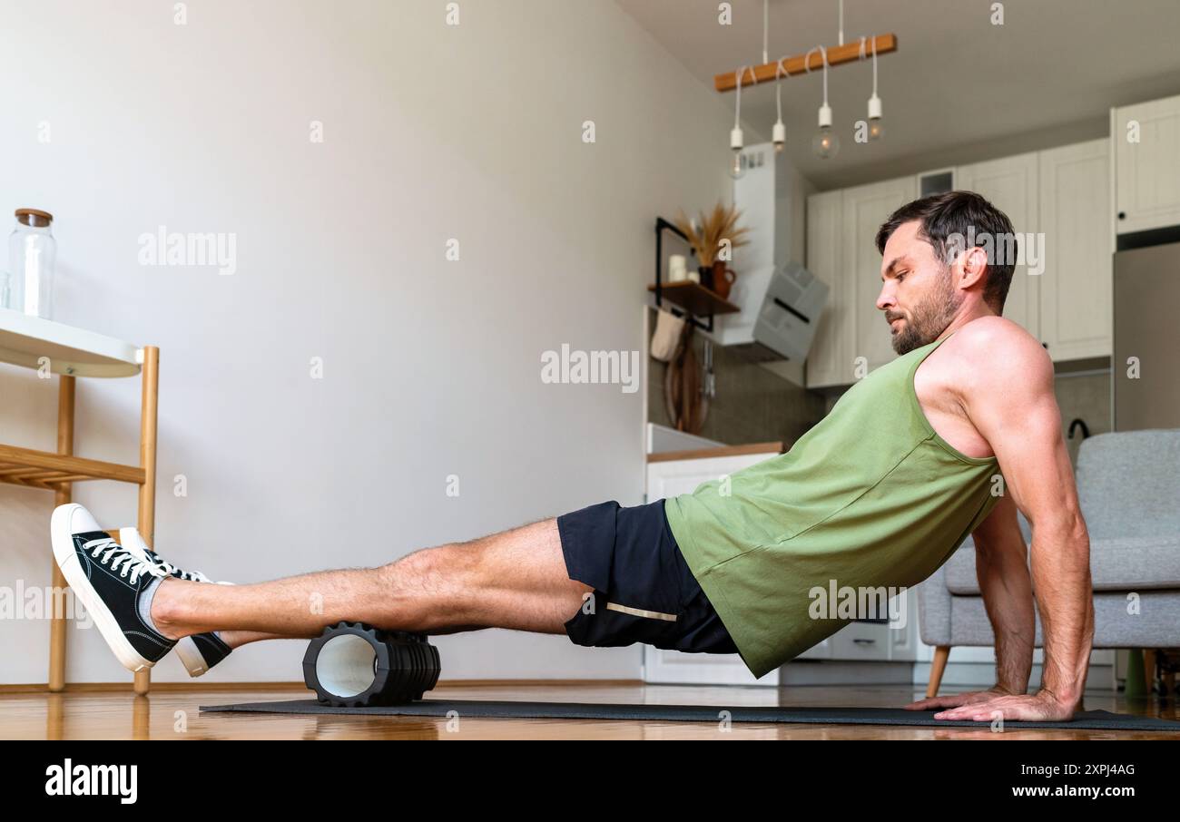 Uomo che esegue un esercizio di rilascio auto-miofasciale a casa utilizzando un rullo in schiuma. Foto Stock