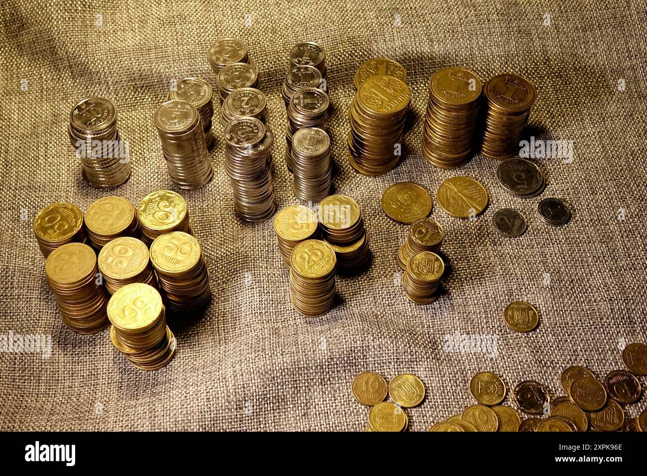 Una collezione di moderne monete ucraine per la circolazione è meticolosamente disposta in colonne ordinate su una superficie in tessuto testurizzato. Le monete variano in dimensioni e d Foto Stock