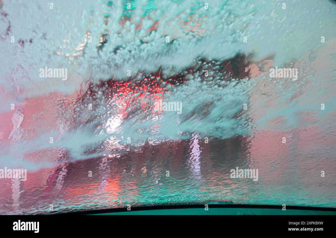 Il parabrezza di un'auto che passa attraverso un autolavaggio automatico. La finestra viene coperta di sapone quando il ciclo di risciacquo inizia a rimuoverla. Foto Stock