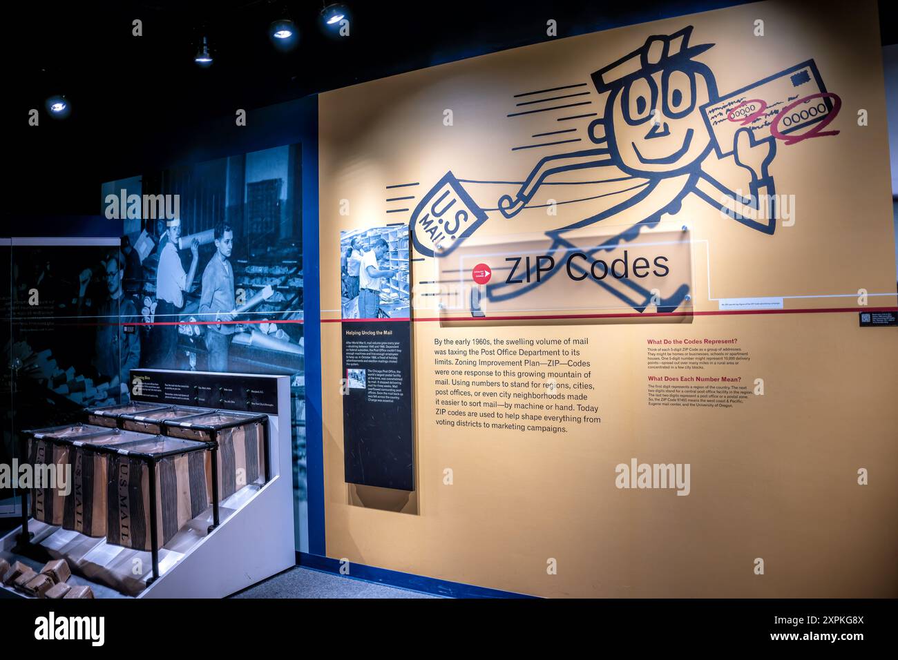 National Postal Museum ZIP Codes Exhibit Washington DC | WASHINGTON D.C., Stati Uniti — Una galleria dedicata ai codici postali presso lo Smithsonian National Postal Museum traccia l'origine del sistema a cinque cifre che ha riorganizzato la posta americana. Introdotto nel 1963 come piano di miglioramento della suddivisione in zone, i codici consentono a macchine e impiegati di ordinare rapidamente un volume di posta in aumento per regione, città e quartiere. I cestini postali in tela vintage e le fotografie d'archivio ancorano il display. Foto Stock