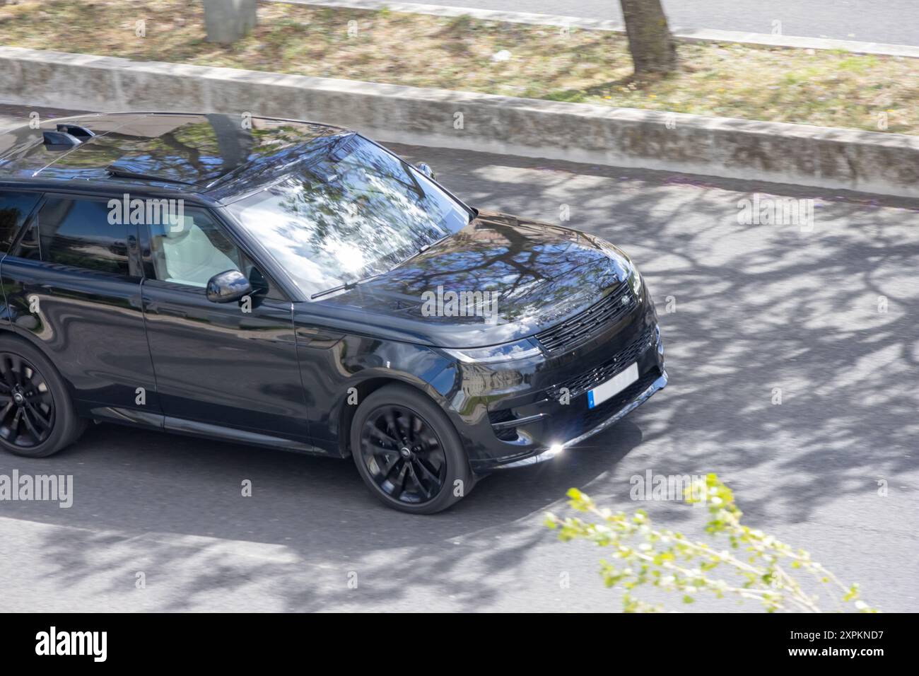 Range rover nera che guida in una giornata di sole, riflettendo gli alberi sui finestrini Foto Stock