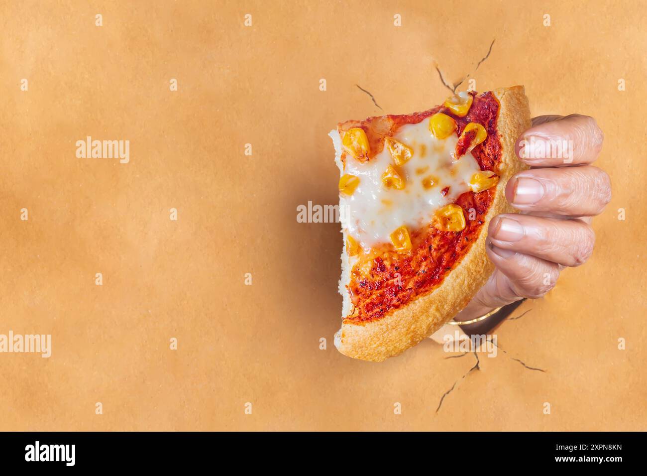 Mano di una donna indiana che tiene una fetta di pizza che esce dopo aver strappato la carta marrone con spazio per il testo. Foto Stock
