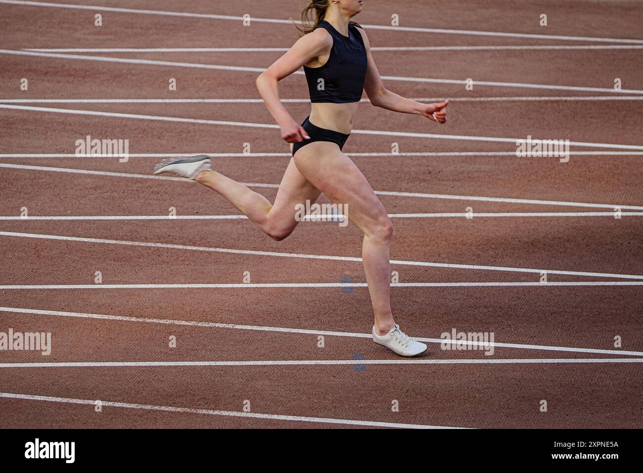 atleta femminile che corre in sprint sullo sfondo di una pista che incrocia le linee di marcatura Foto Stock