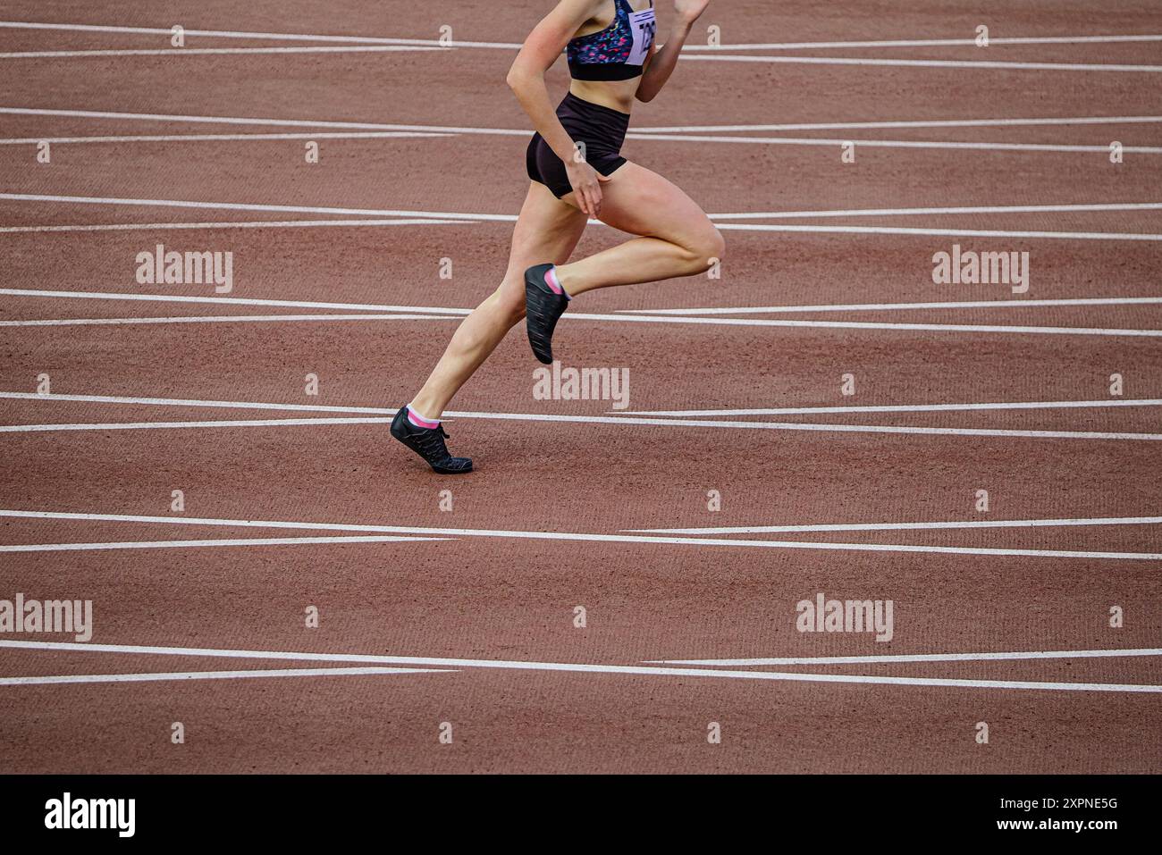 atleta donna che corre da stadio sullo sfondo di una pista che si incrocia con linee di marcatura Foto Stock