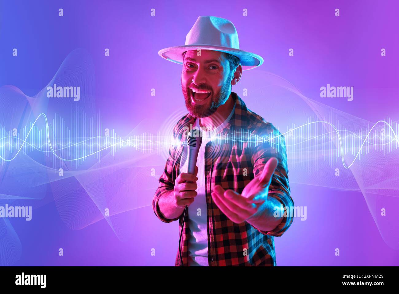 Uomo emotivo con microfono che canta nelle luci al neon. Forme d'onda audio vicino a lui Foto Stock
