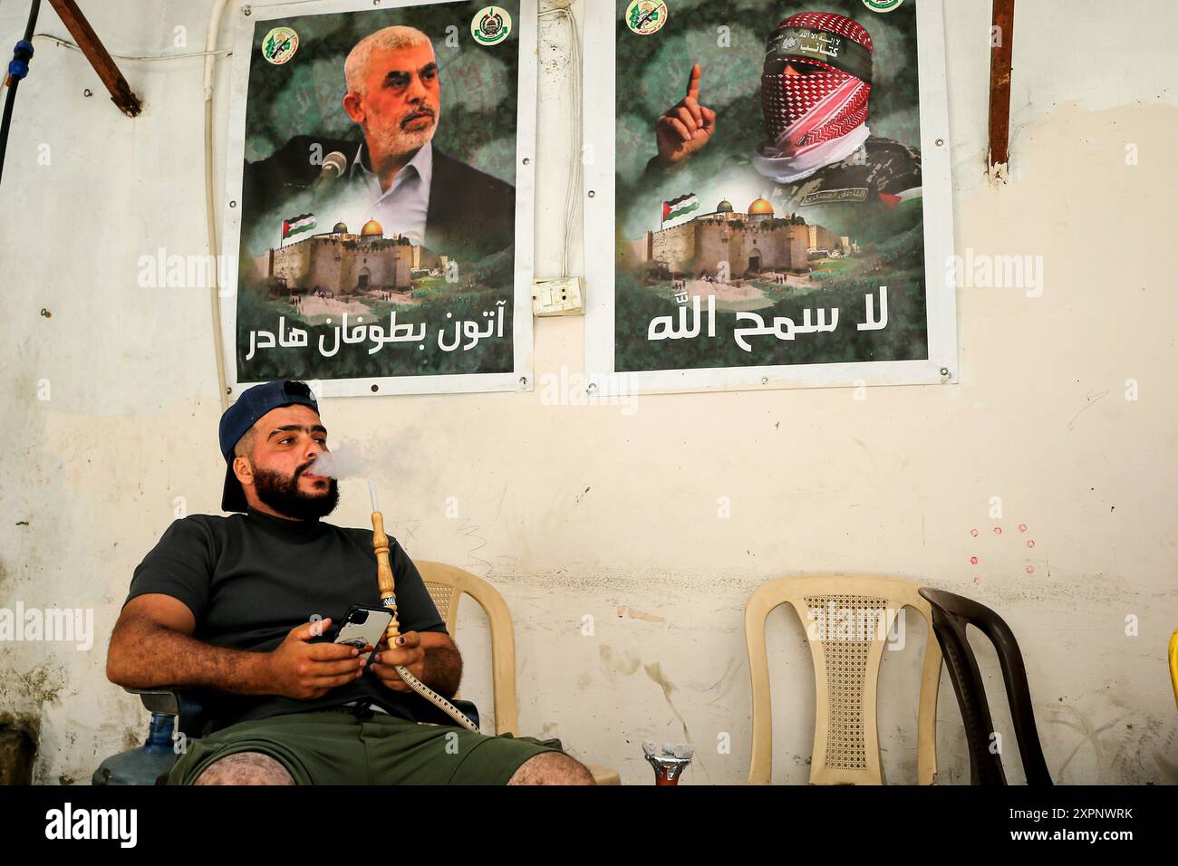 Beirut, Libano. 7 agosto 2024. Un palestinese fuma shisha in un caffè di strada a Beirut, campo profughi di Burj al-Barjneh, decorato con immagini di Yehya al-Sinwar (L), il capo di Hamas nella Striscia di Gaza, che è stato scelto per sostituire il defunto Ismail Haniyeh come leader del gruppo militante palestinese. Haniyeh, con sede in Qatar, è stato assassinato quasi una settimana fa in un attacco incolpato Israele mentre visitava Teheran per l'insediamento del nuovo presidente iraniano. Crediti: Marwan Naamani/dpa/Alamy Live News Foto Stock