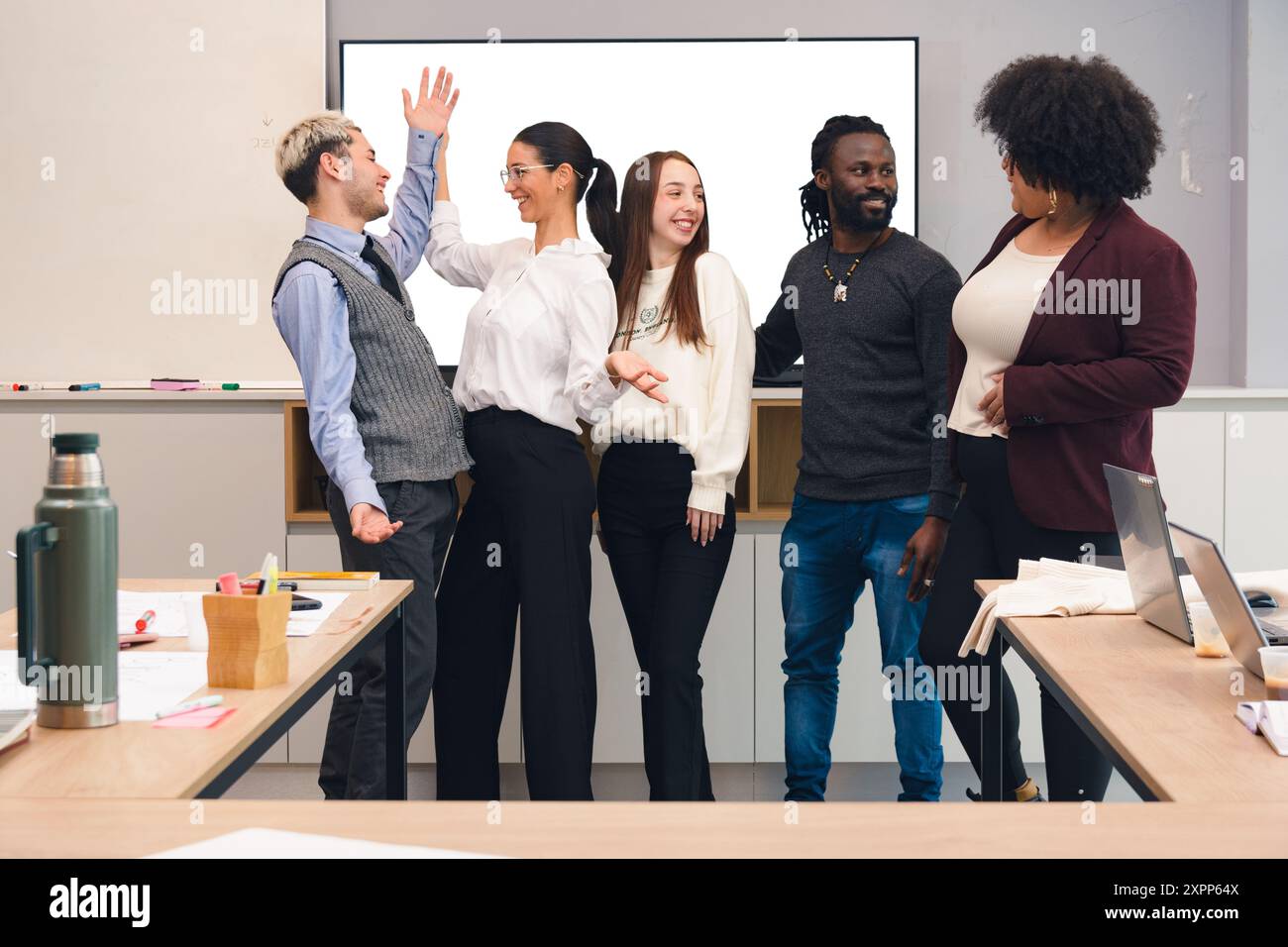 I giovani di diverse razze ed etnie sono distratti dal parlare durante il lavoro in ufficio, ridono e parlano tra di loro Foto Stock