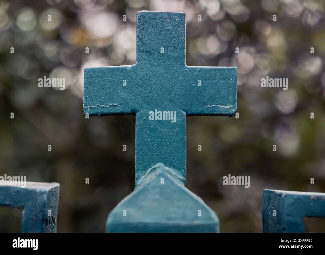 Foto ravvicinata di una croce cristiana su una recinzione verde ferro su uno sfondo sfocato in un ambiente naturale con effetto bokeh Foto Stock